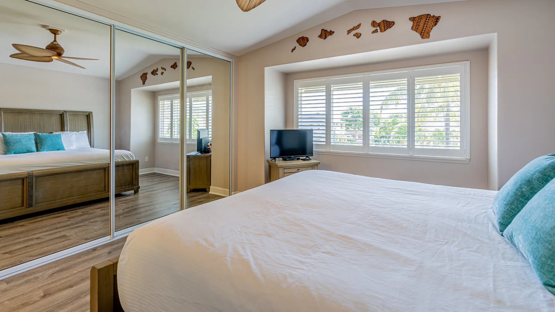 Un dormitorio con una cama, puertas de armario con espejos y ventanas amplias.