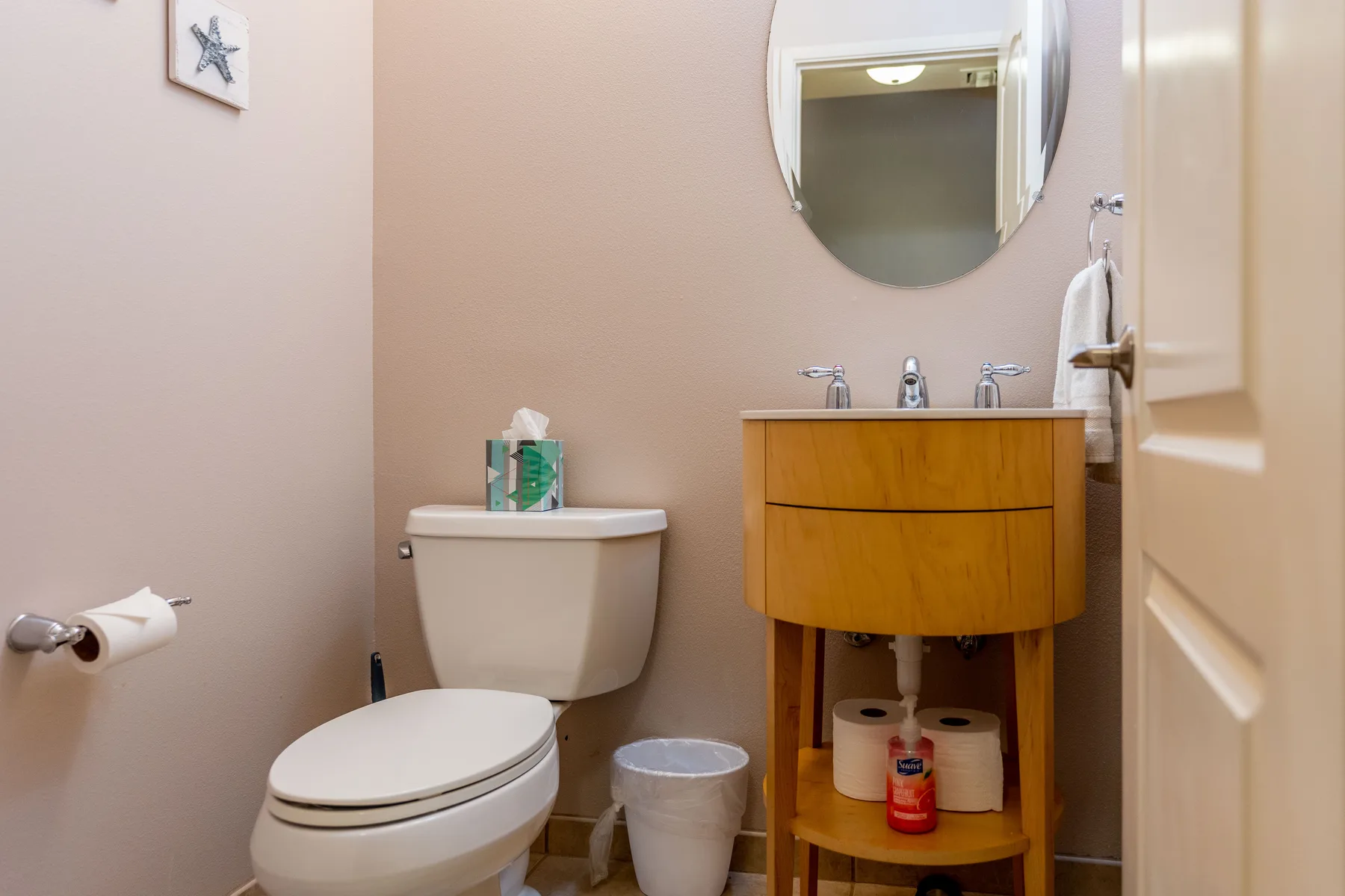 Un baño con un inodoro, un tocador de madera y un espejo redondo.
