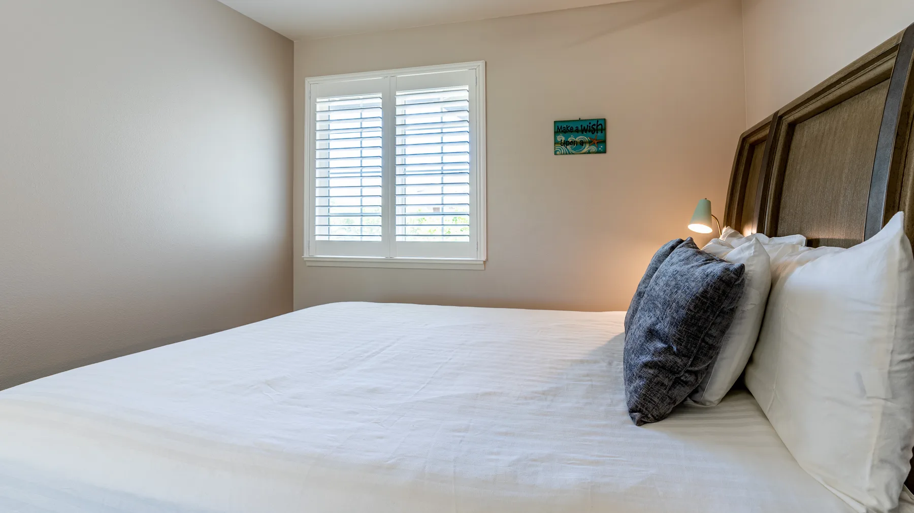 Un dormitorio con una cama bien tendida, almohadas y una ventana con persianas.