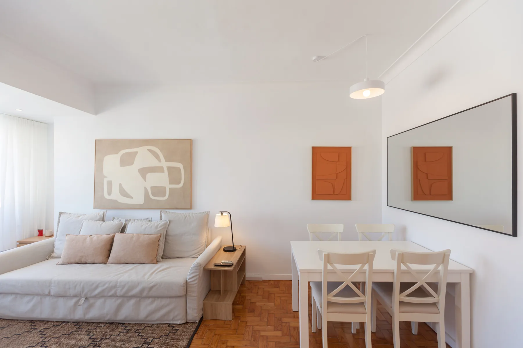 A bright living and dining area with a sofa, table, and wall art.