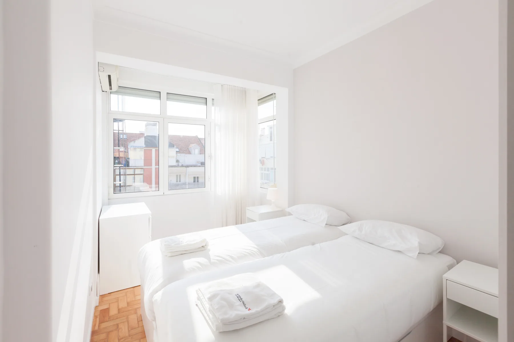 A bright bedroom with white bedding and large windows.
