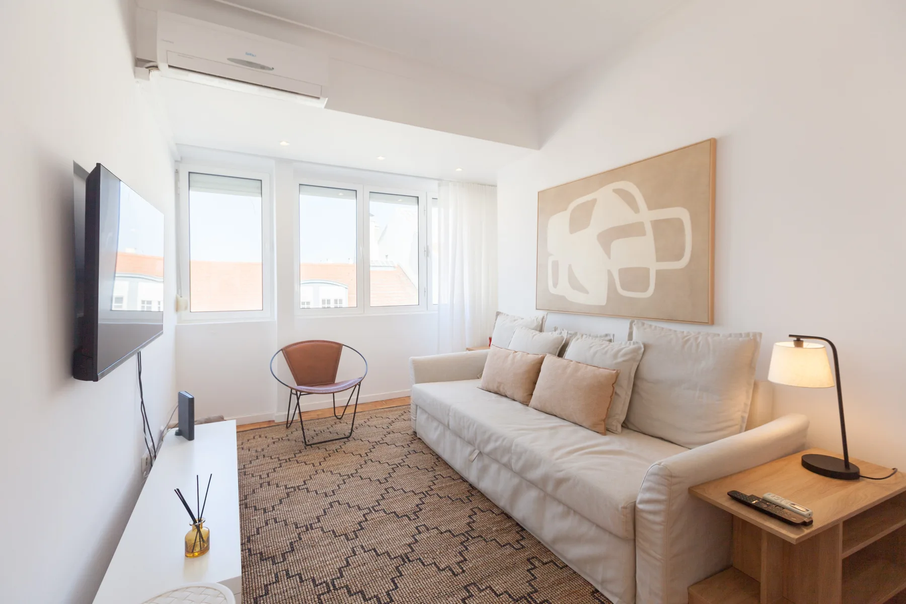 A bright living room with seating, a patterned rug, and large windows.