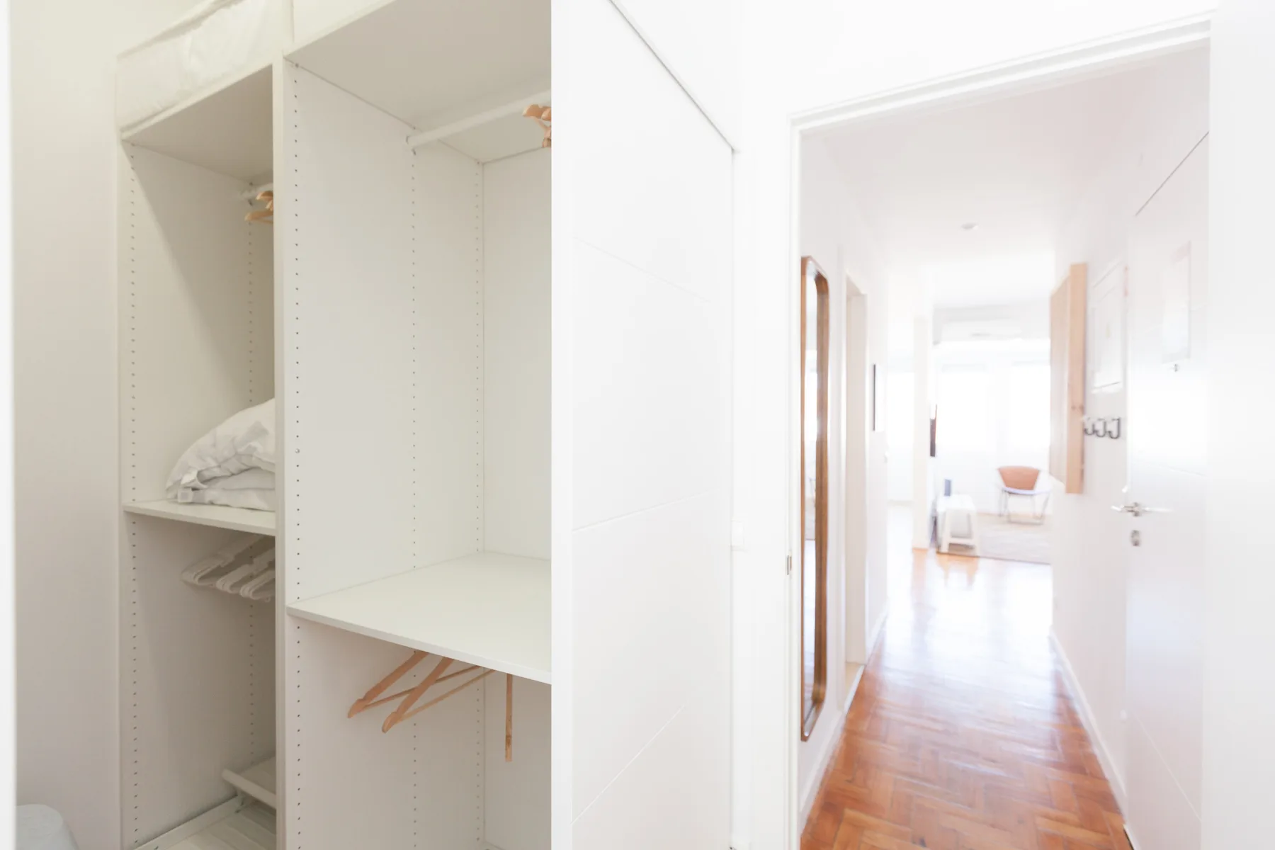 An open closet with shelves and hangers beside a bright hallway.