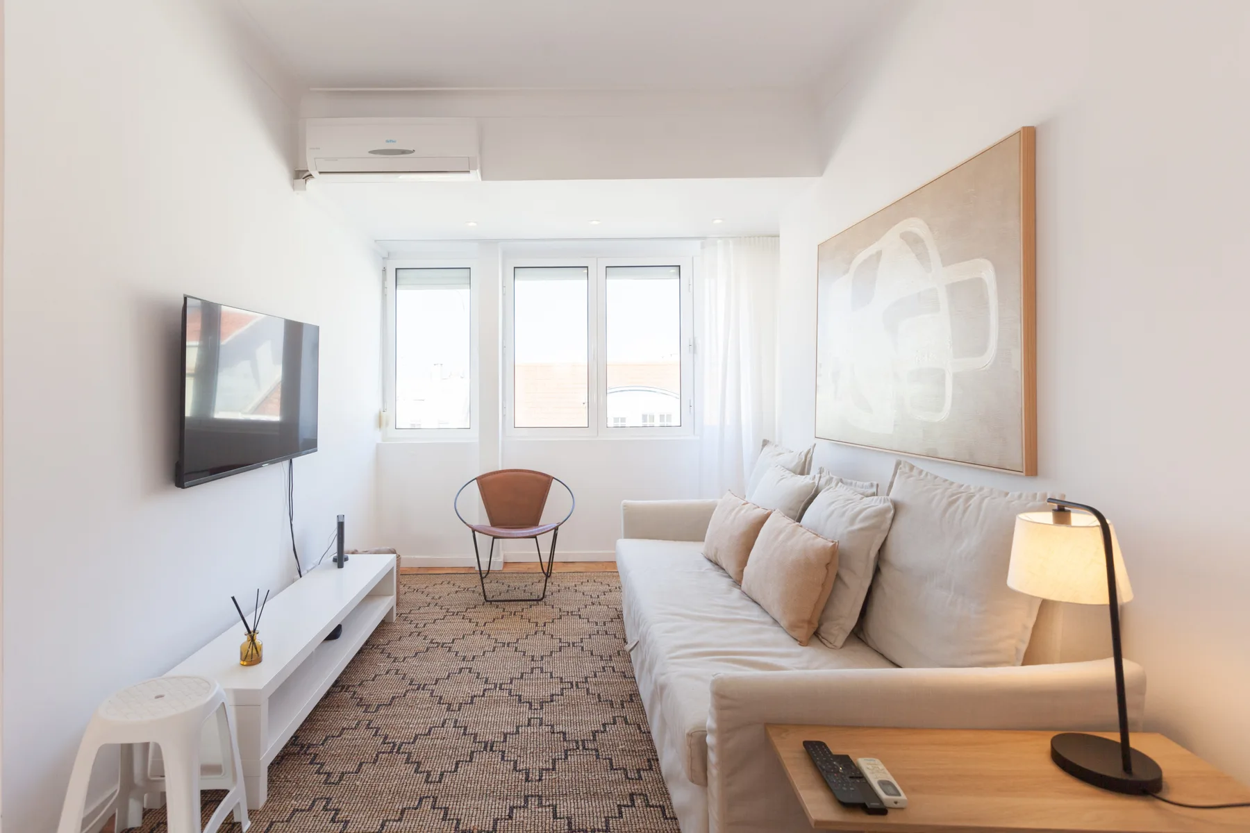A bright living room with seating, a television, and large windows.
