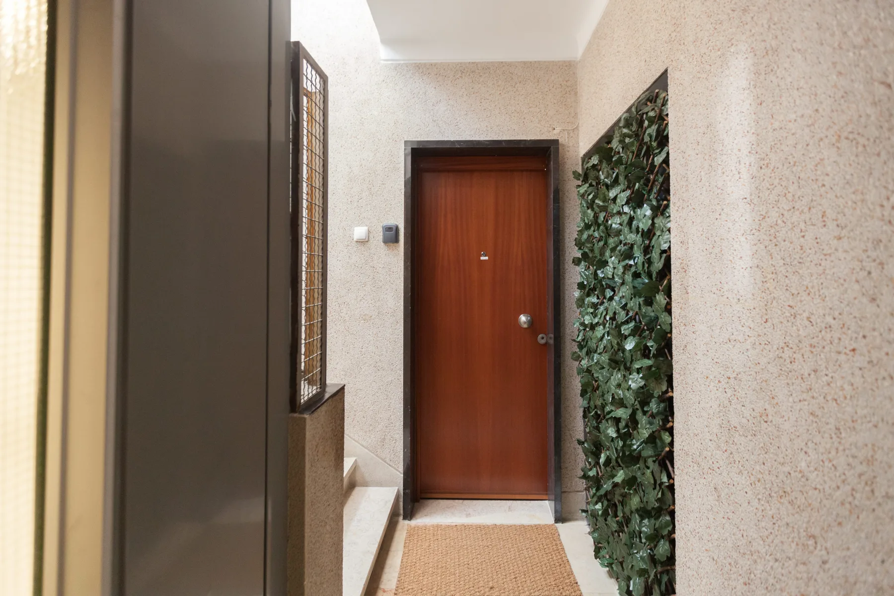 An apartment entryway with a wooden door and a leafy wall panel.