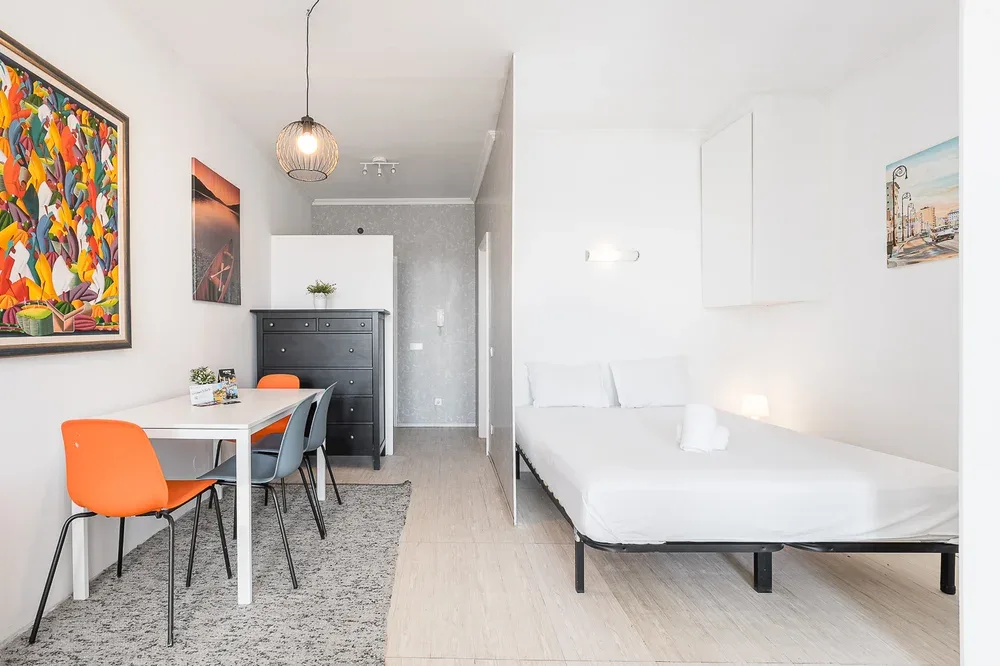 A bright bedroom with a bed, a dining table, and colorful wall art.