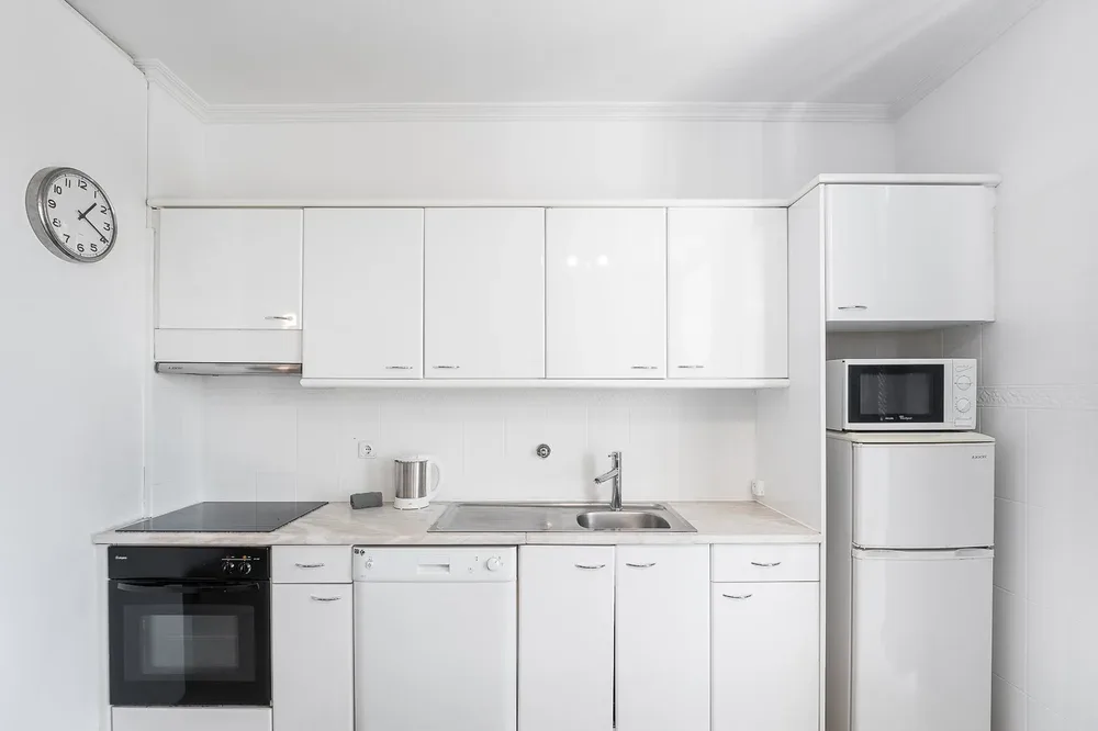 A bright white kitchen with cabinets, a countertop, and built-in appliances.