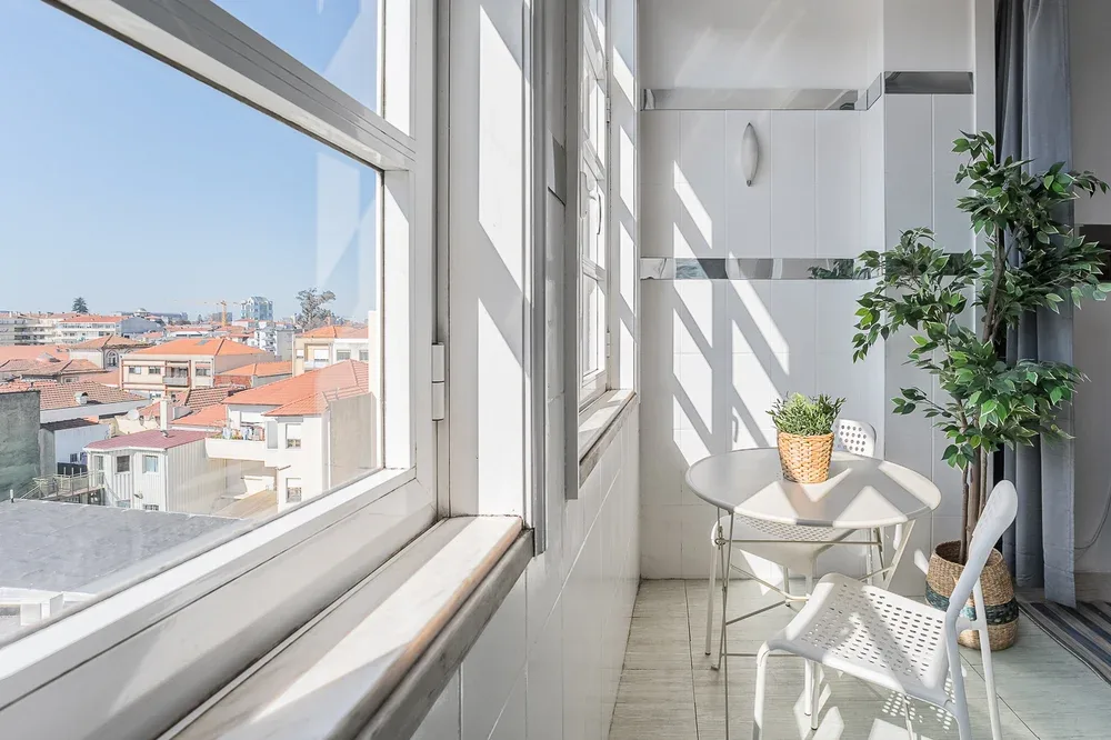 A bright enclosed balcony with a small table, chairs, and a potted plant.
