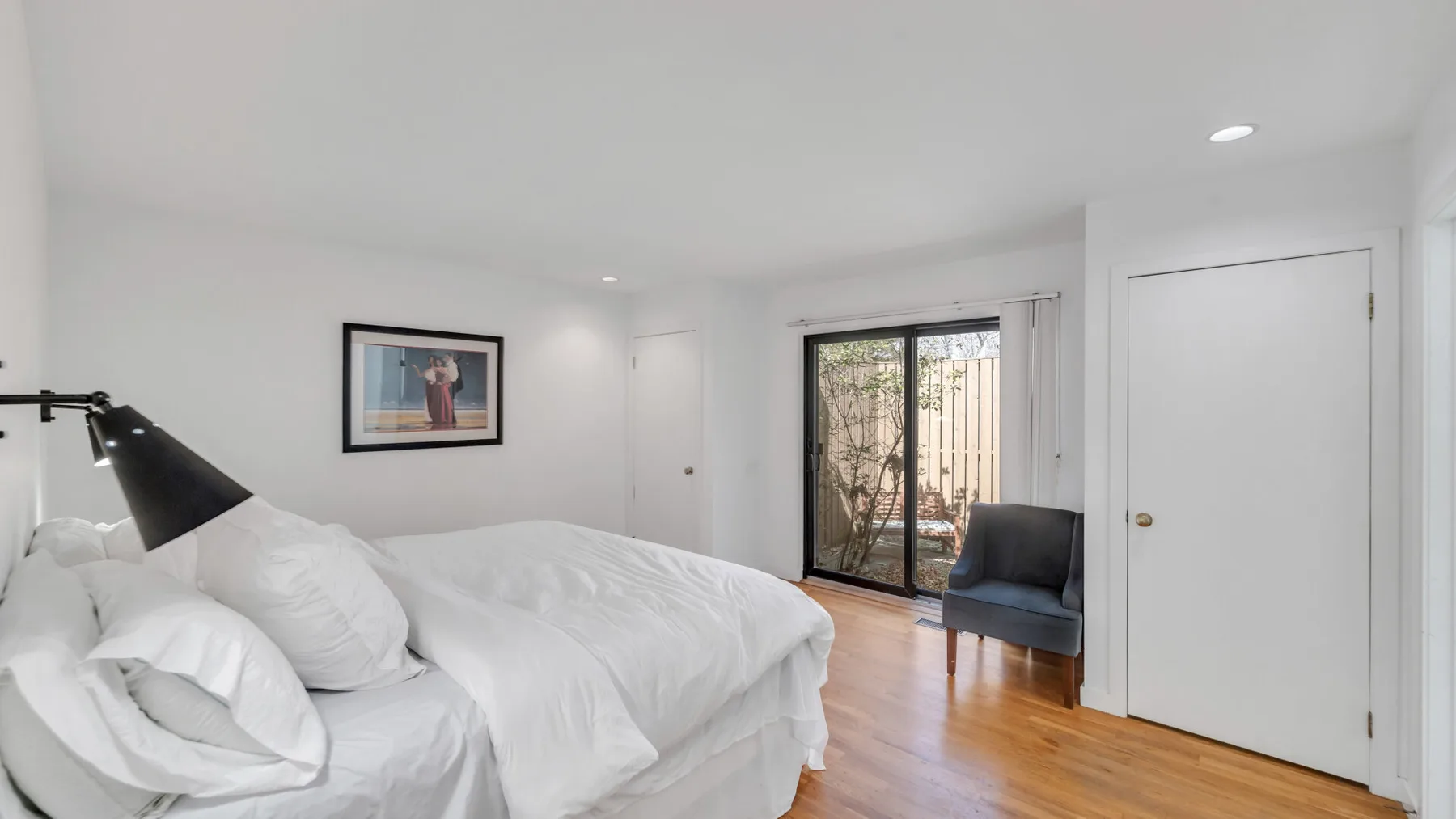 A bright bedroom with white bedding, a framed picture, and a glass door to the patio.