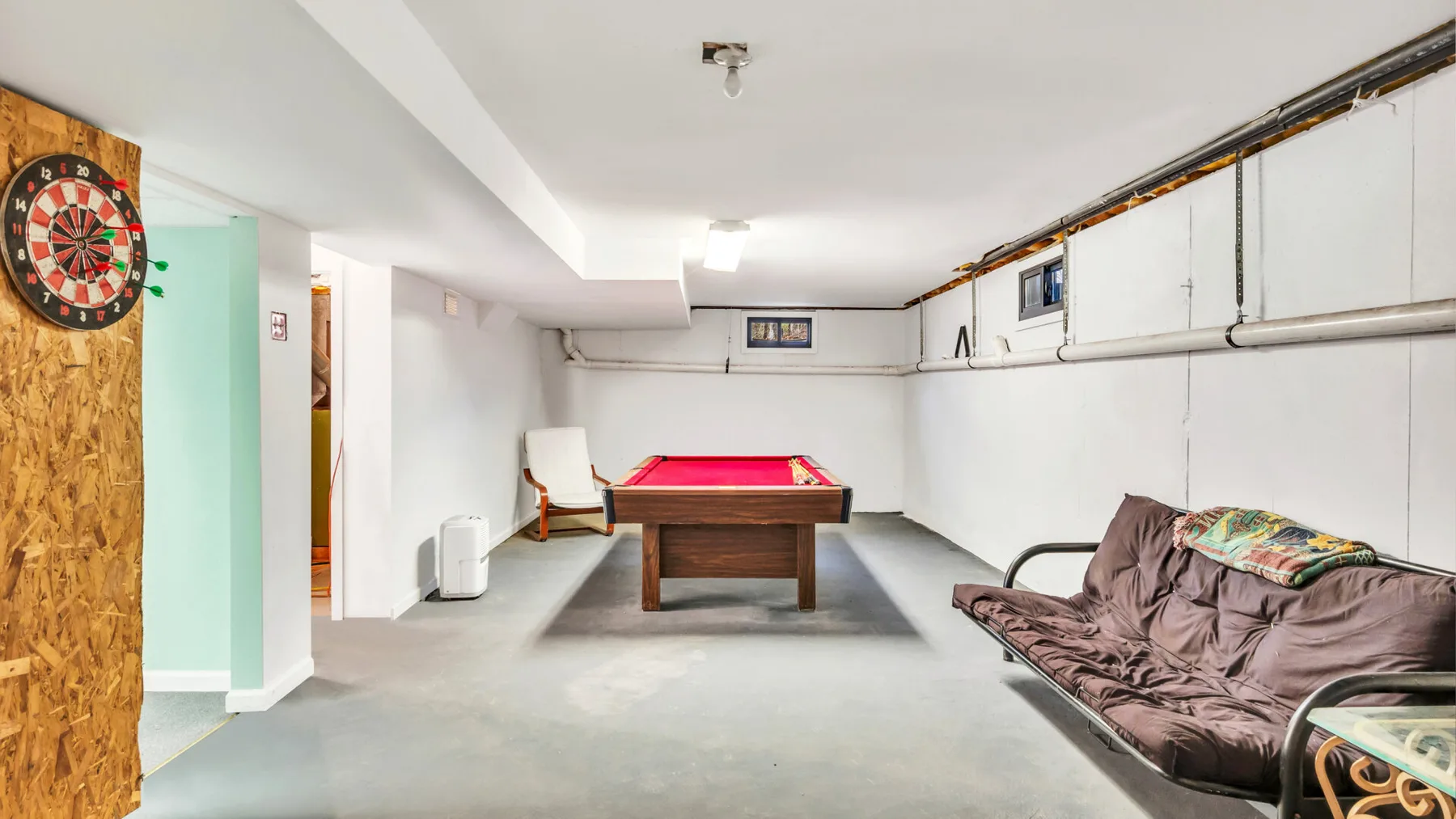A basement game room with a pool table, dartboard, and seating.