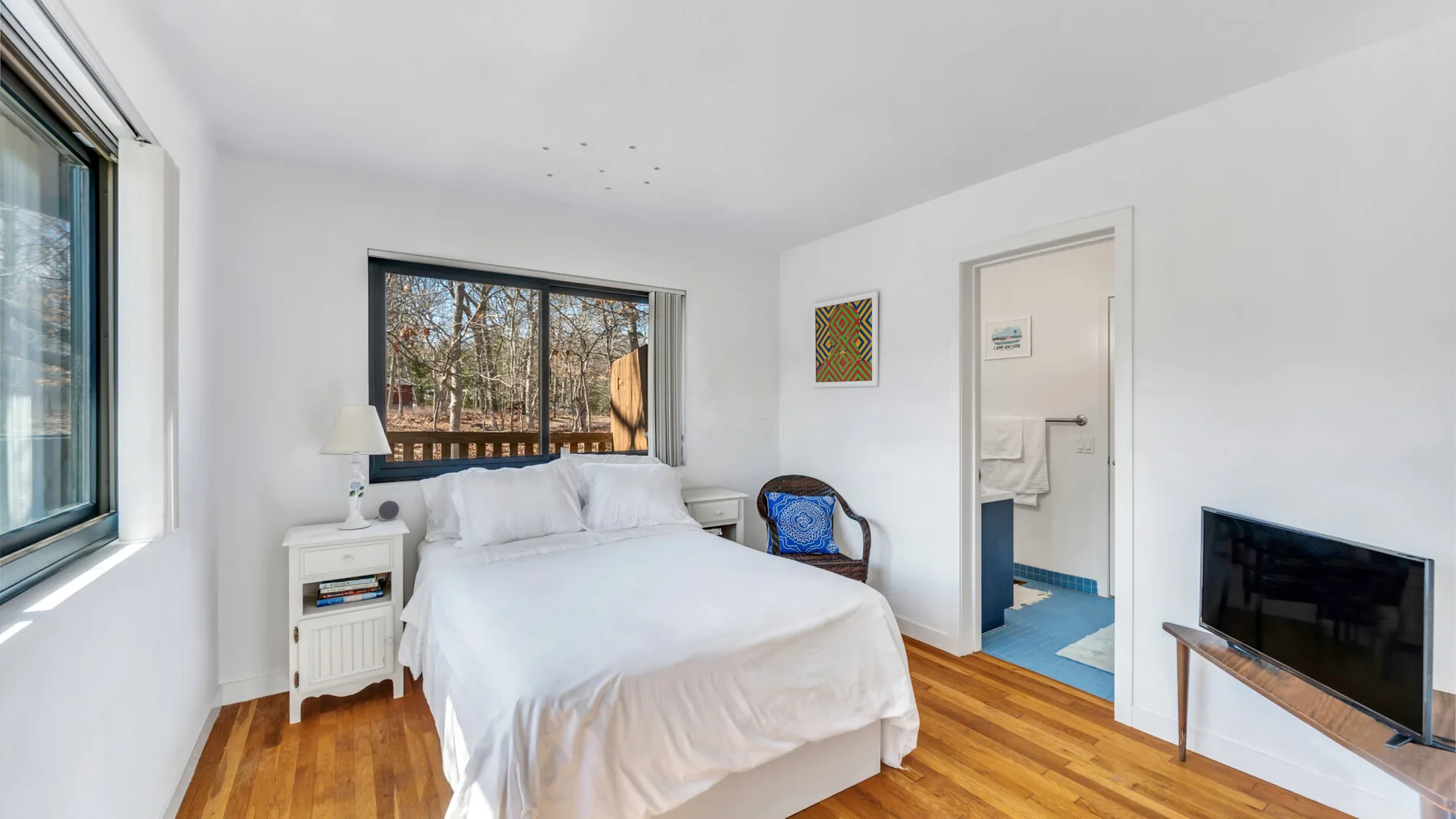 A bright bedroom with a neatly made bed, wood flooring, and a television.
