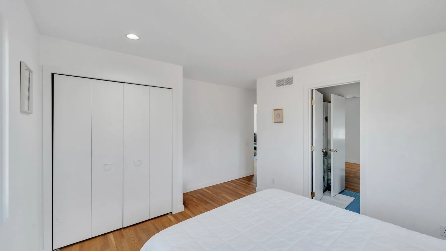 A bright bedroom with white closet doors and wooden flooring.