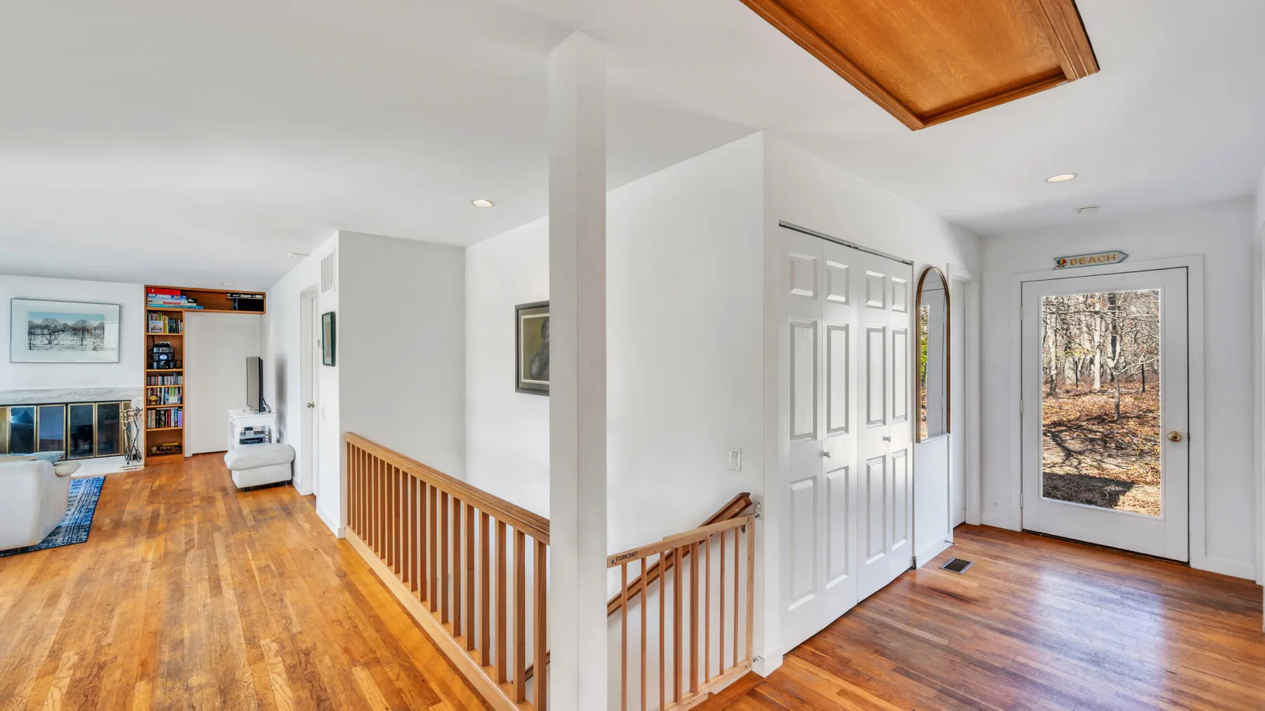 A bright upstairs hallway with wooden flooring, a railing, and a glass-paneled door.