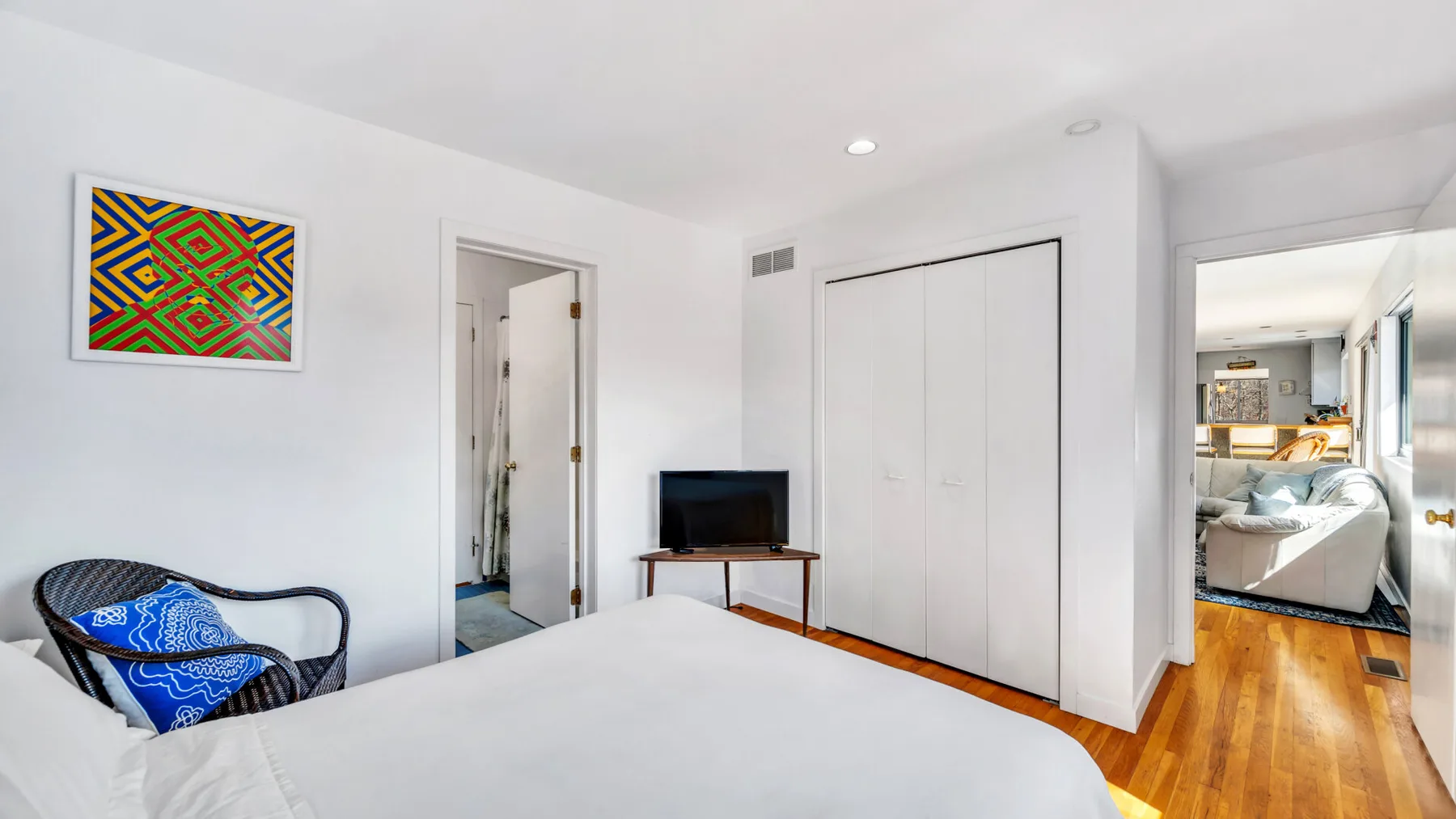 A bright bedroom with a bed, wall art, and a television on a stand.
