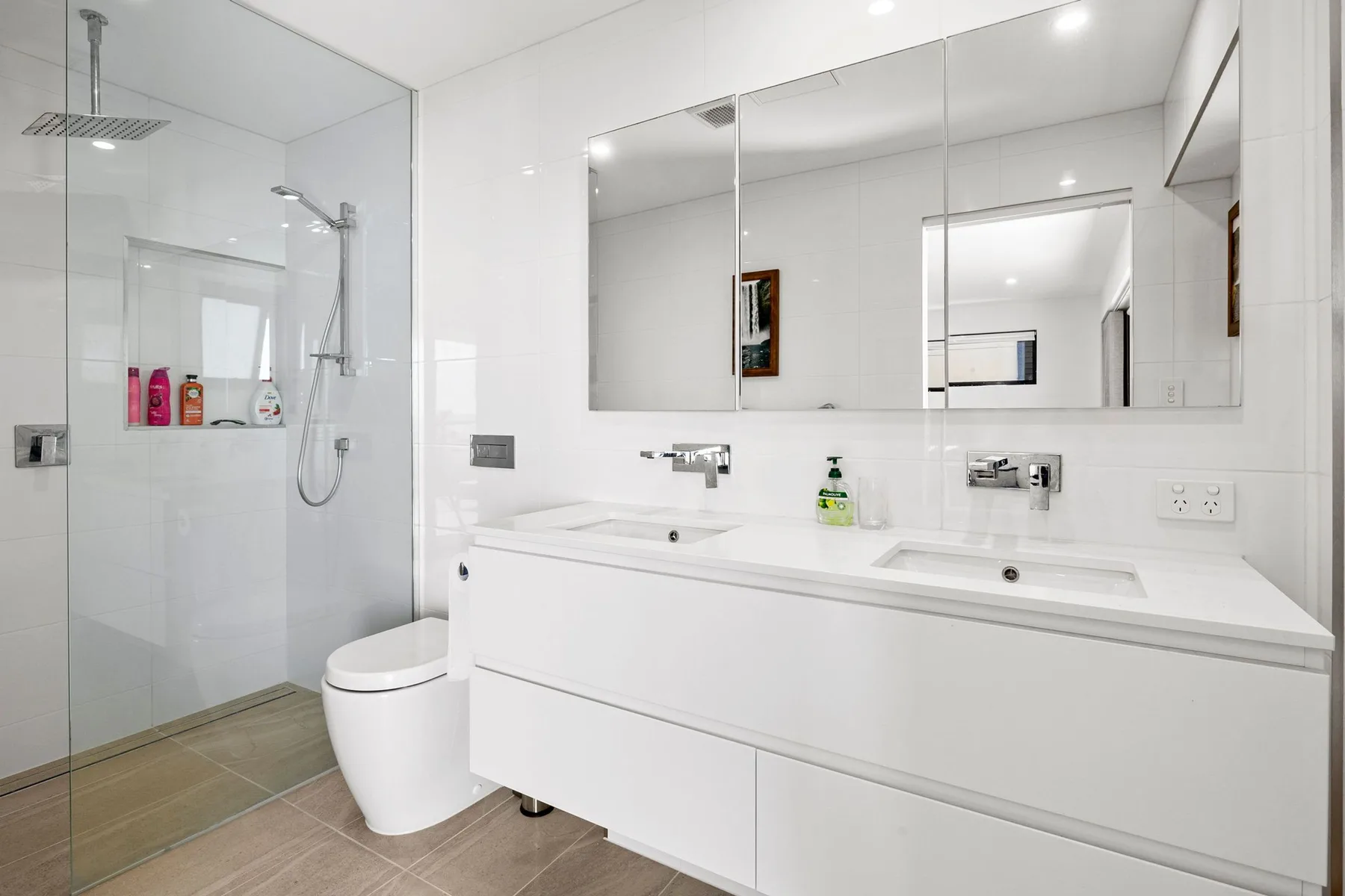 Un baño luminoso con ducha de vidrio, inodoro y lavabo doble.