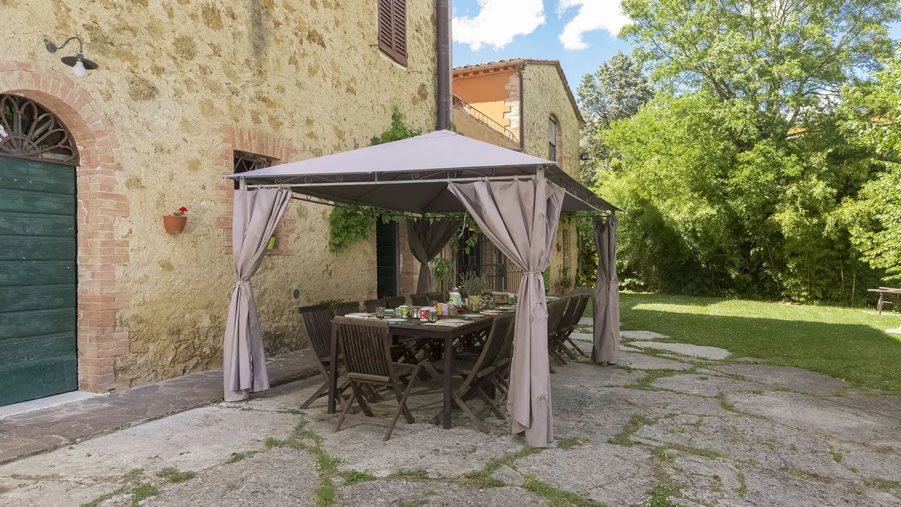 Un edificio de piedra con una zona de comedor al aire libre bajo un toldo junto a un jardín.