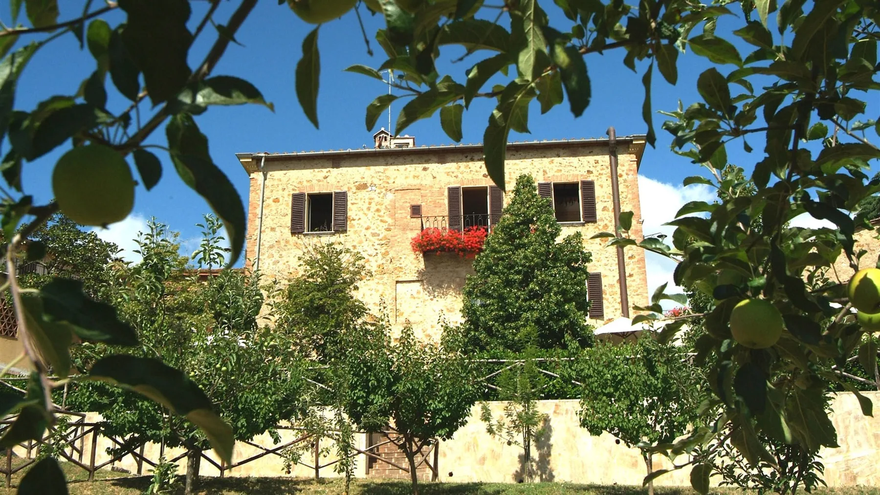 Una casa de piedra está detrás de árboles frondosos y un muro de jardín.