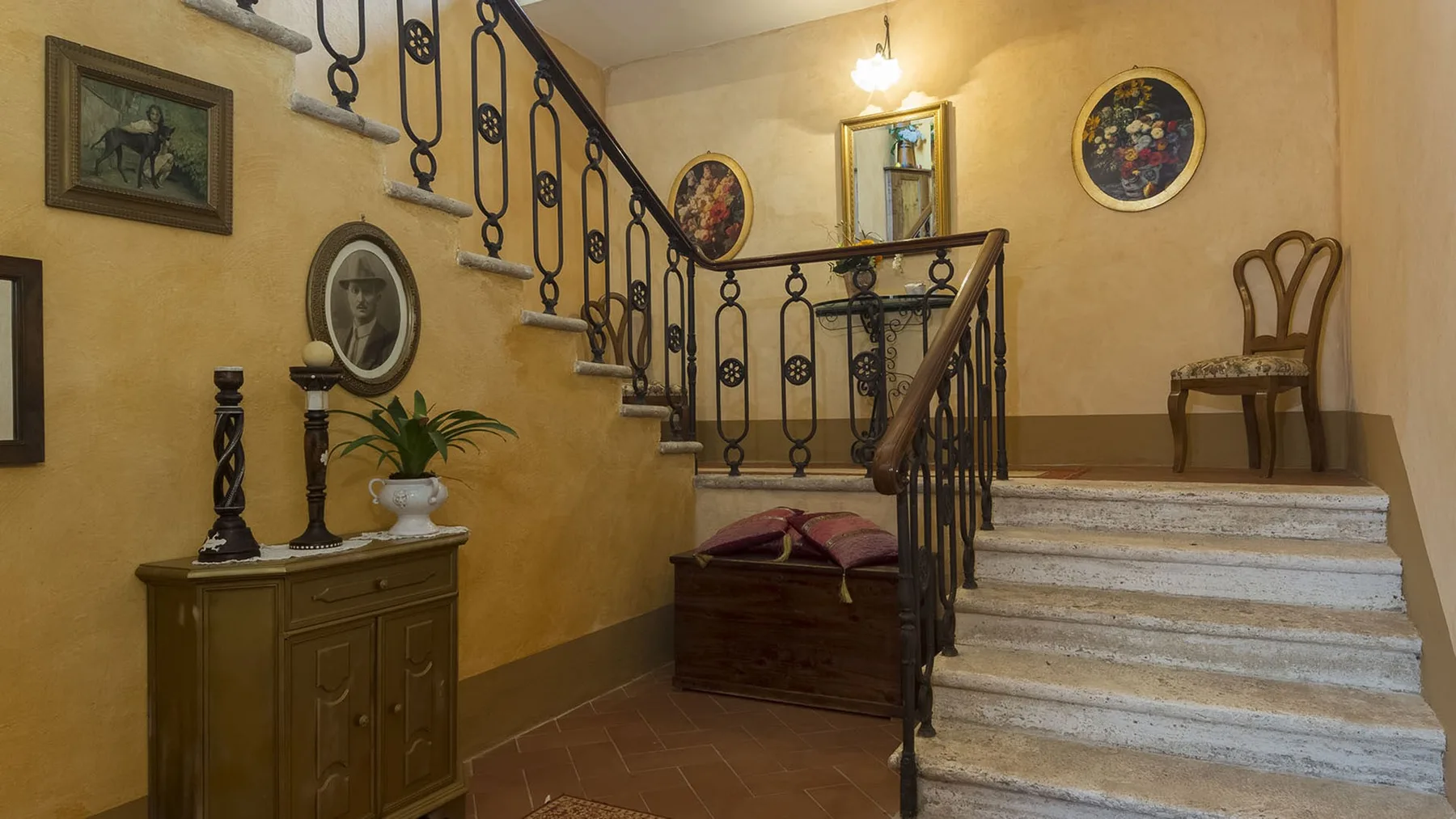 Una escalera interior de tonos cálidos con barandales de hierro decorativos y cuadros en la pared.