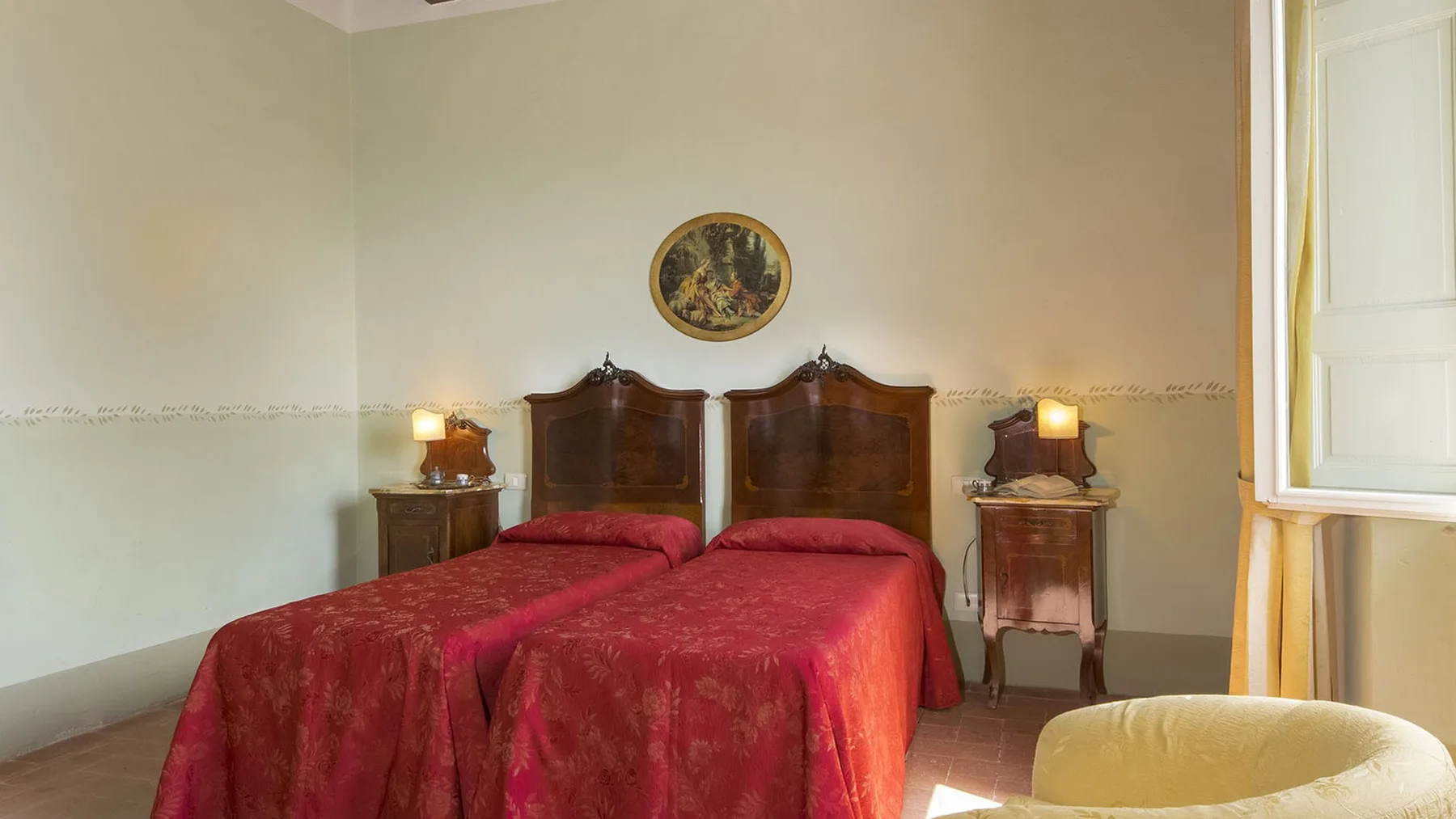 Un dormitorio con dos camas cubiertas con colchas rojas y mesitas a los lados.