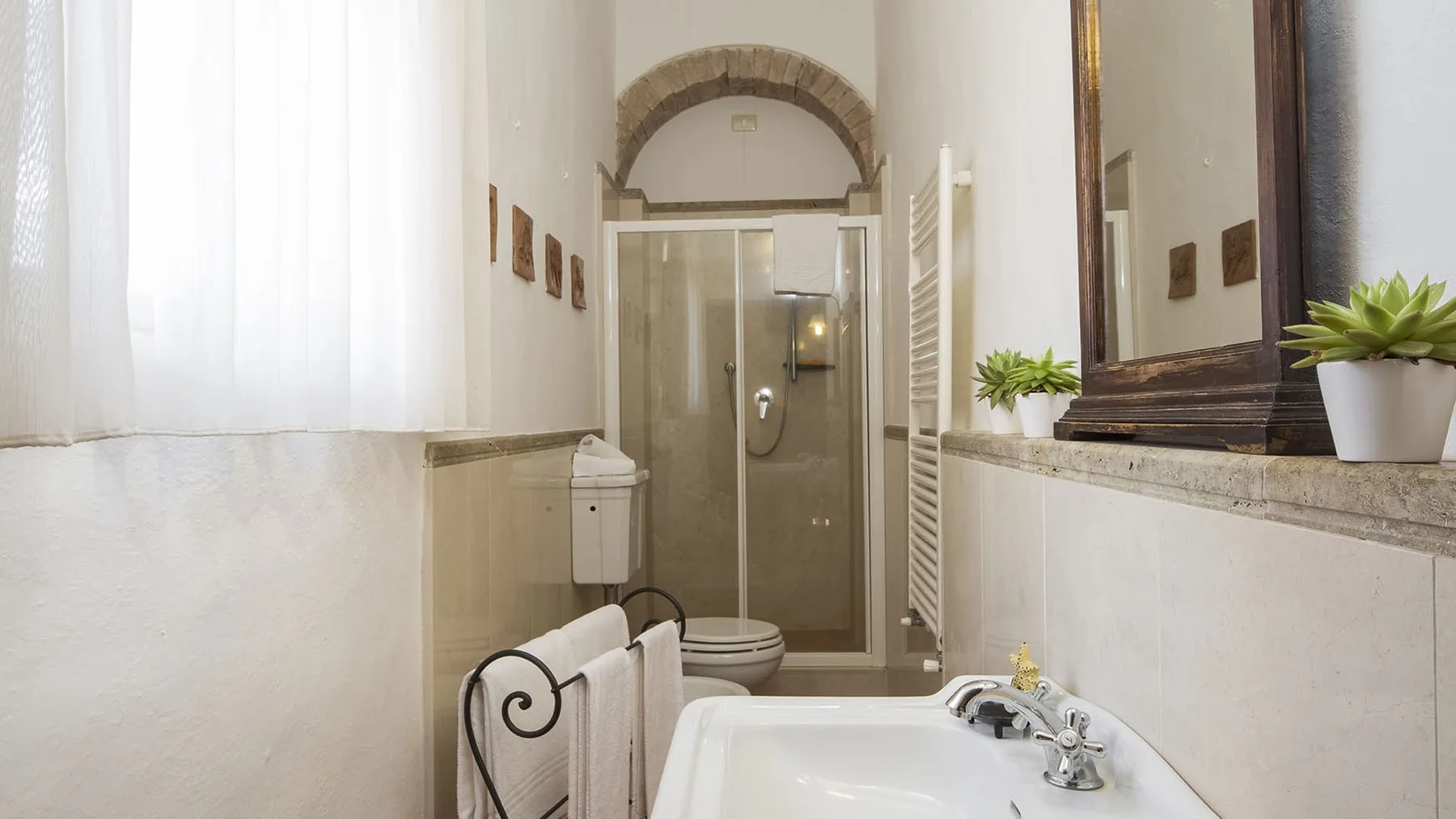 Un baño luminoso con una ducha de vidrio y un lavabo bajo un espejo grande.