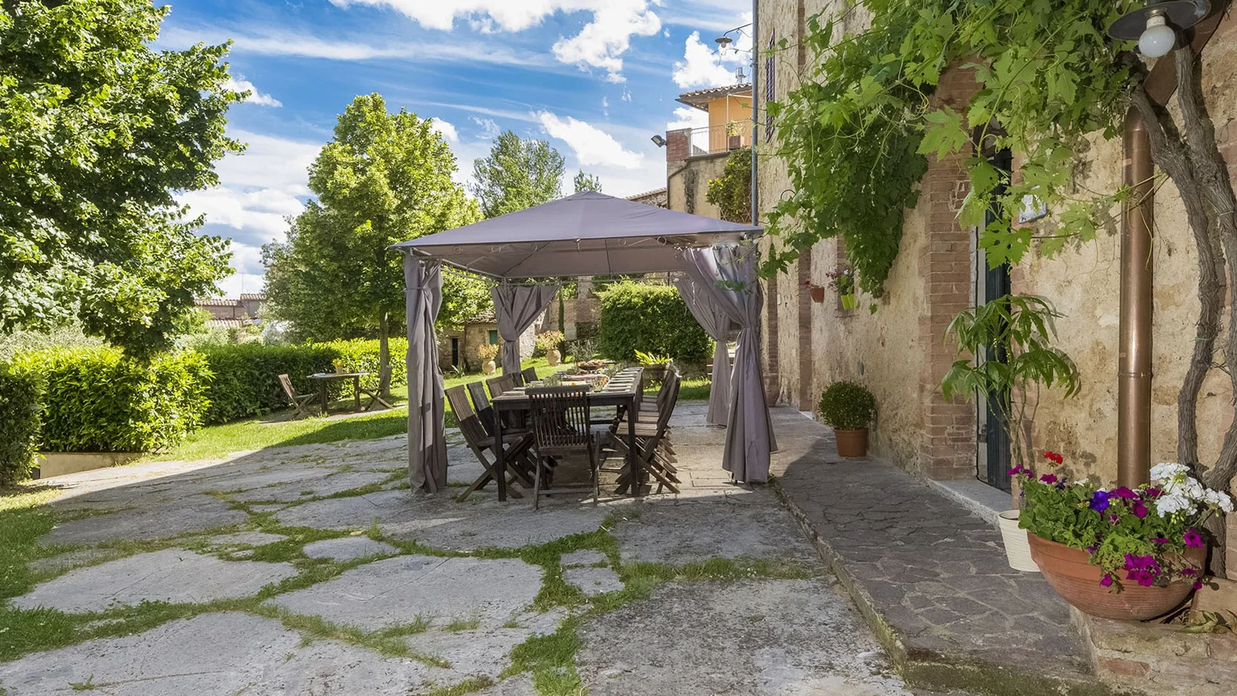 Una zona de comedor al aire libre está bajo un toldo junto a un edificio de piedra.