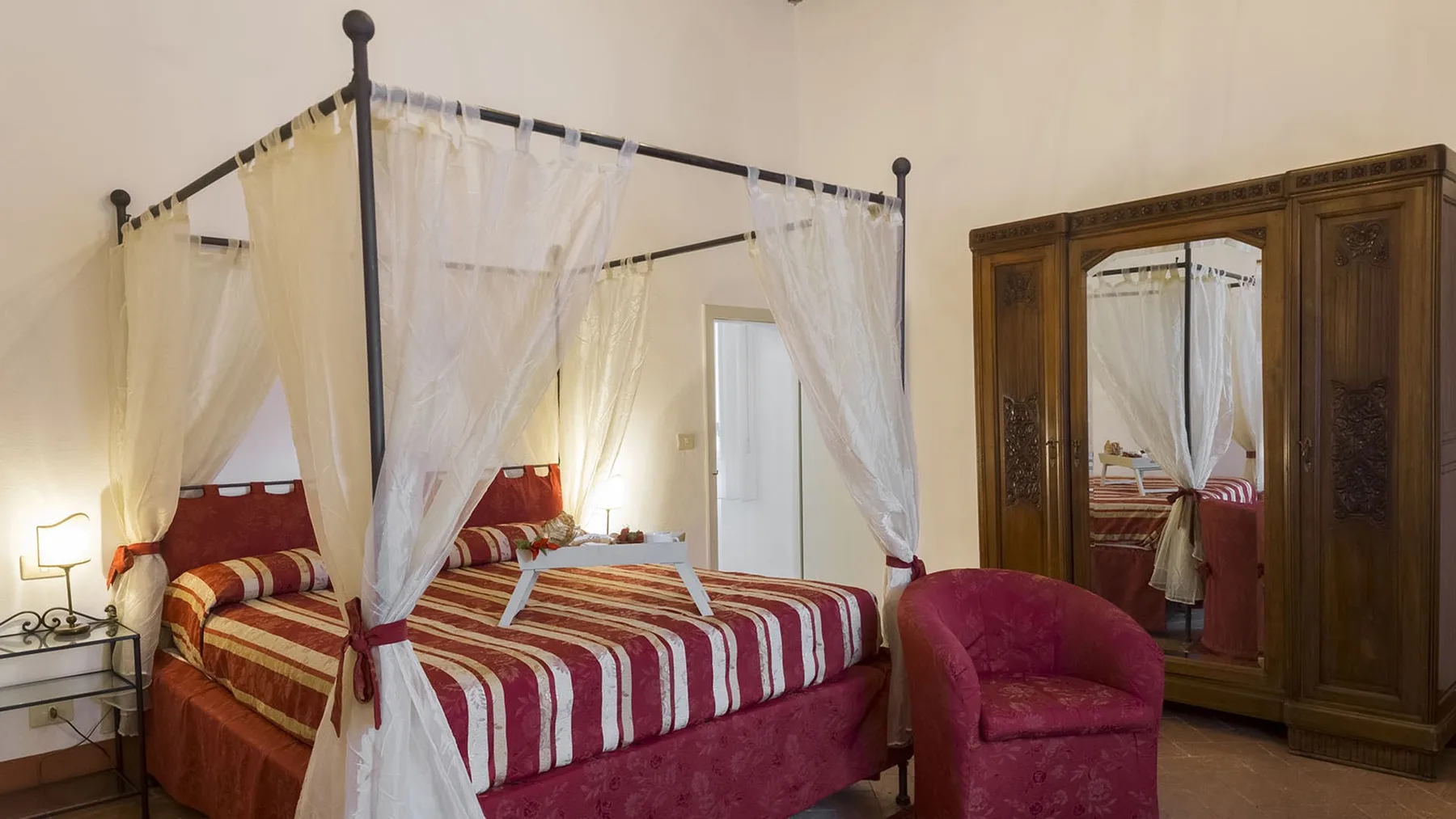 Un dormitorio con una cama a rayas bajo un dosel y un armario de madera.