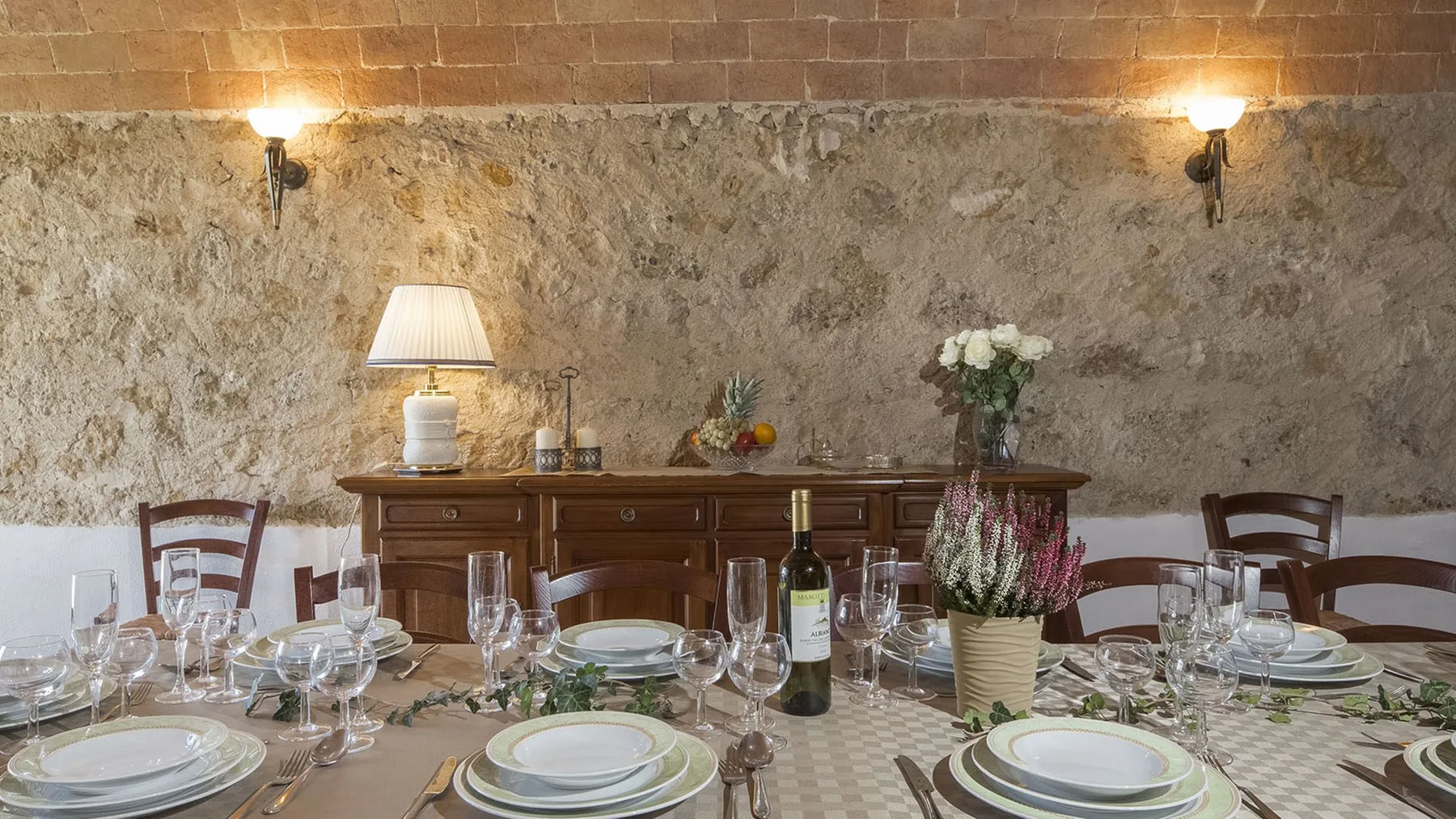 Un comedor está dispuesto con una mesa larga, vajilla y flores.