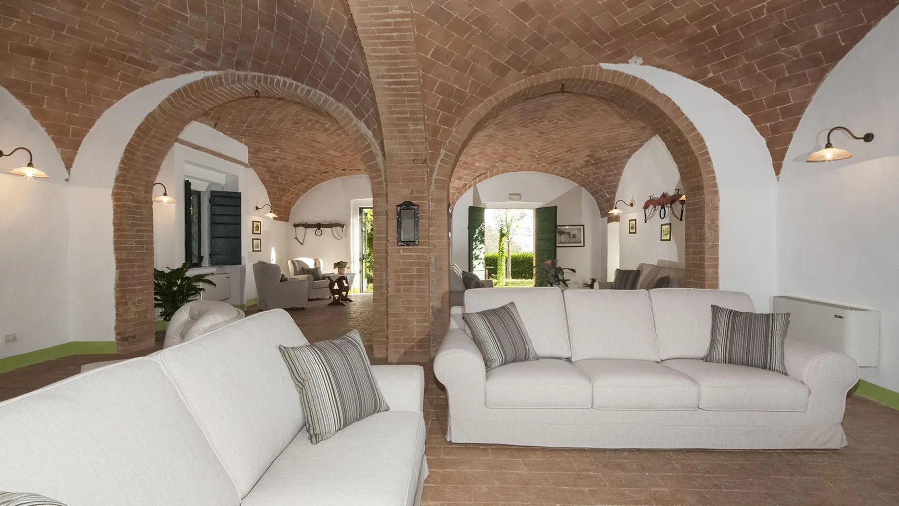 Una sala de estar con asientos blancos bajo arcos y una bóveda de ladrillo.