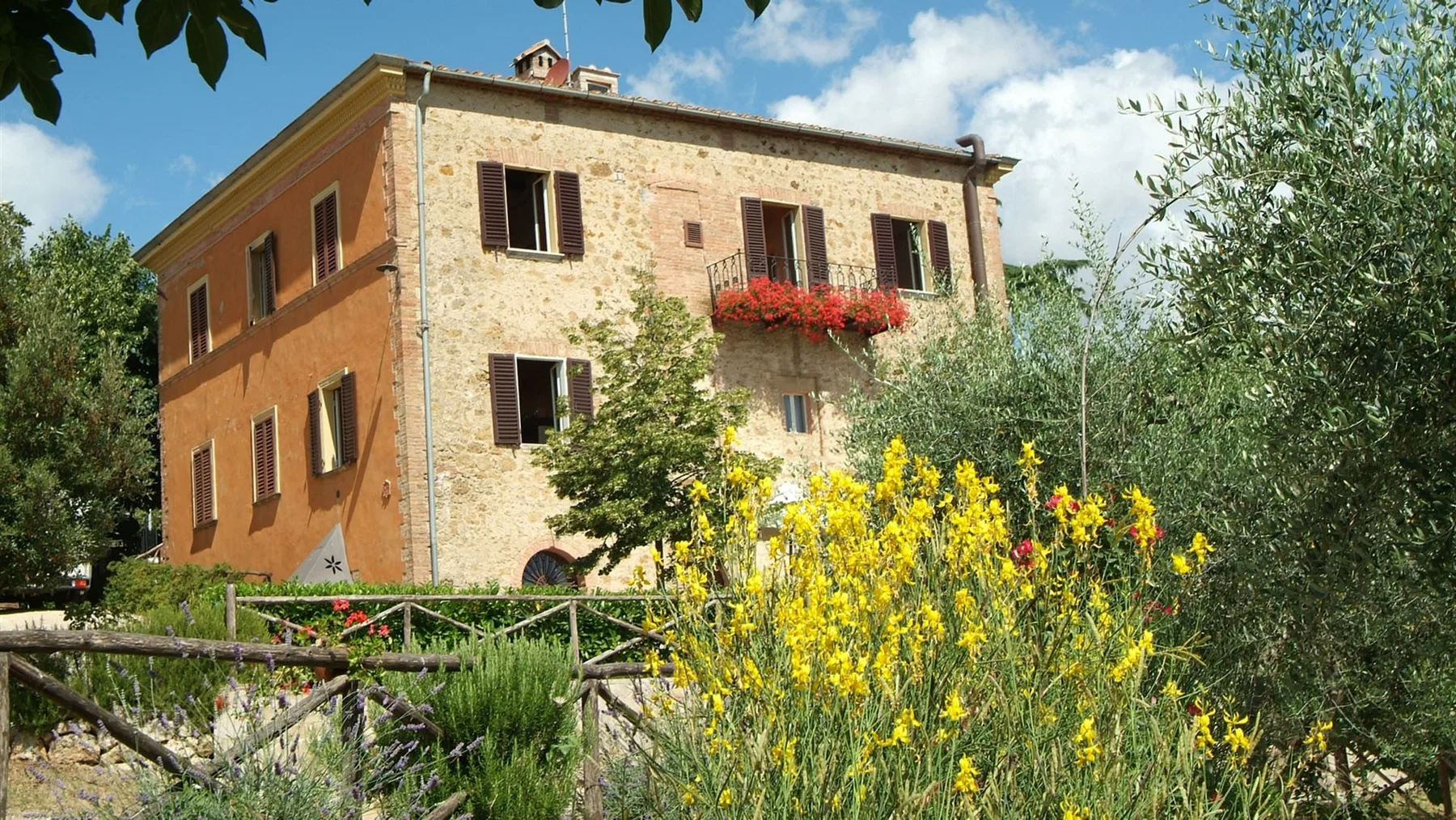 Una casa de piedra se alza detrás de un jardín de flores amarillas.