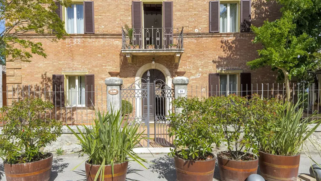 Entrada de un edificio de ladrillo con una verja metálica y plantas frondosas delante.