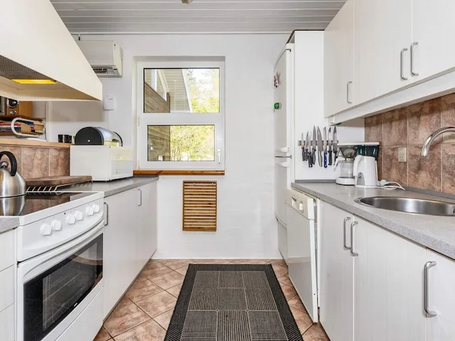 A narrow kitchen with white cabinets, countertops, and a central floor mat.
