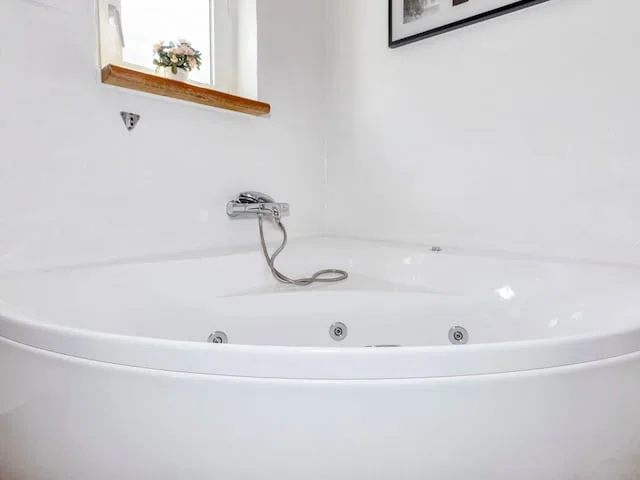 A bathroom with a large white bathtub and wall-mounted faucet.