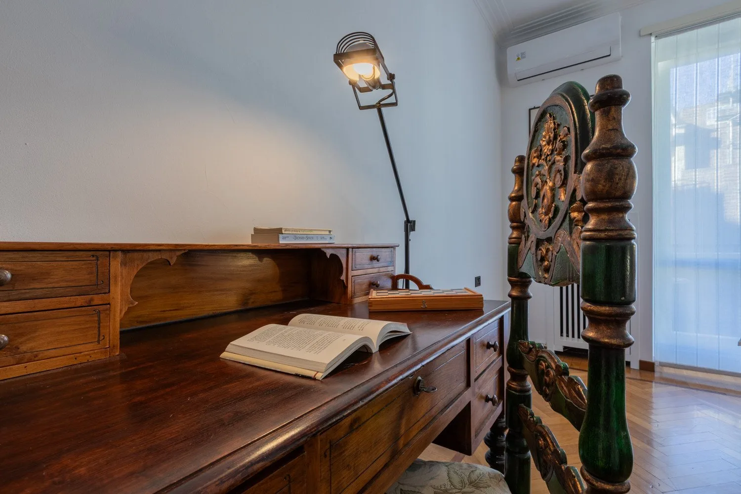 A wooden desk with an open book stands beside an ornate carved bed frame.