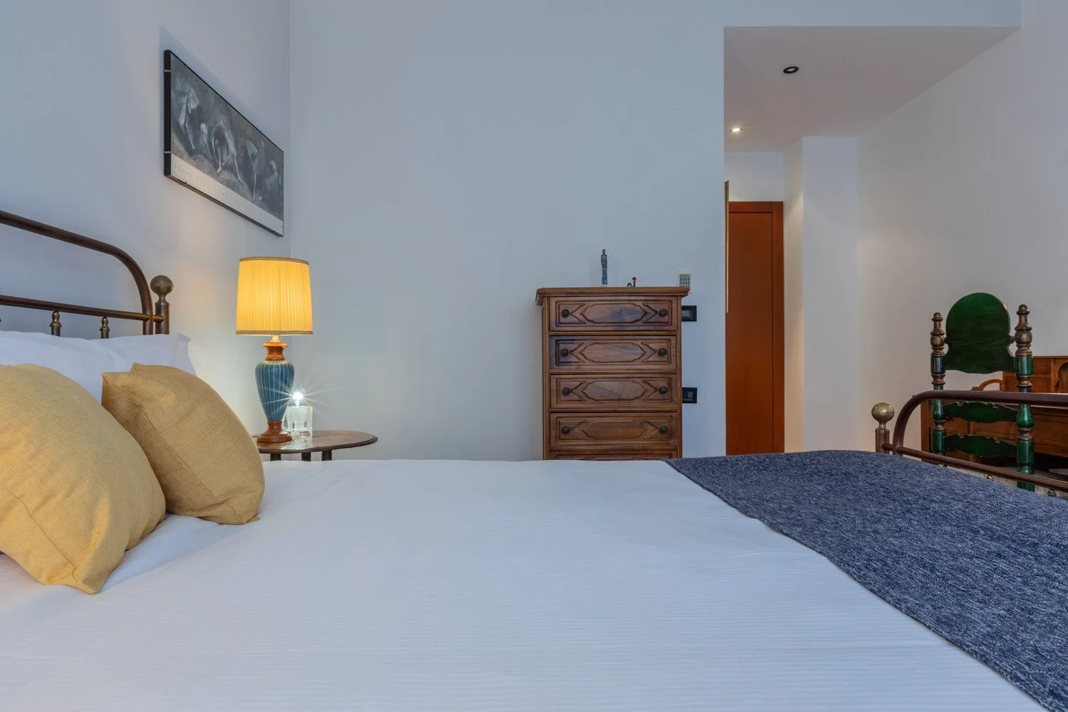 A bedroom with a made bed, bedside lamp, and wooden dresser.