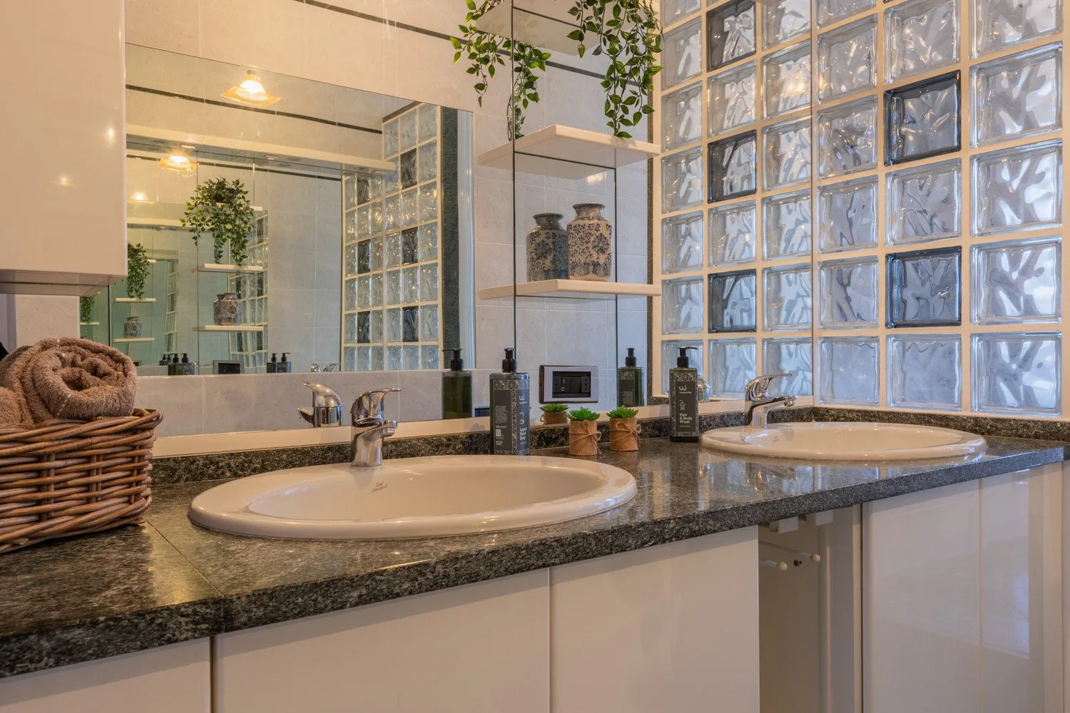 A bathroom vanity with two sinks sits beside a wall of glass blocks.