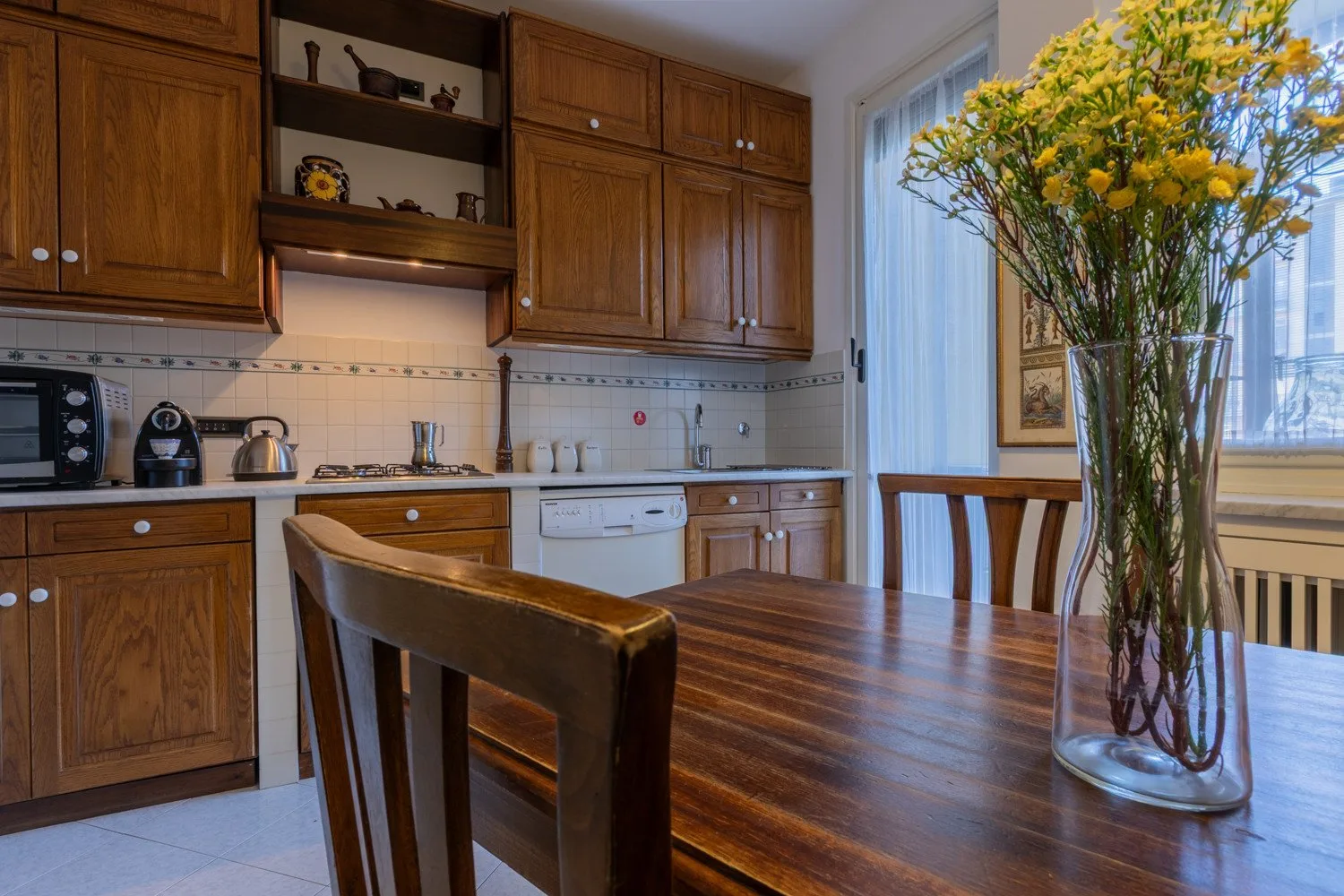 A kitchen dining area with wooden cabinets, a table, and a vase of flowers.