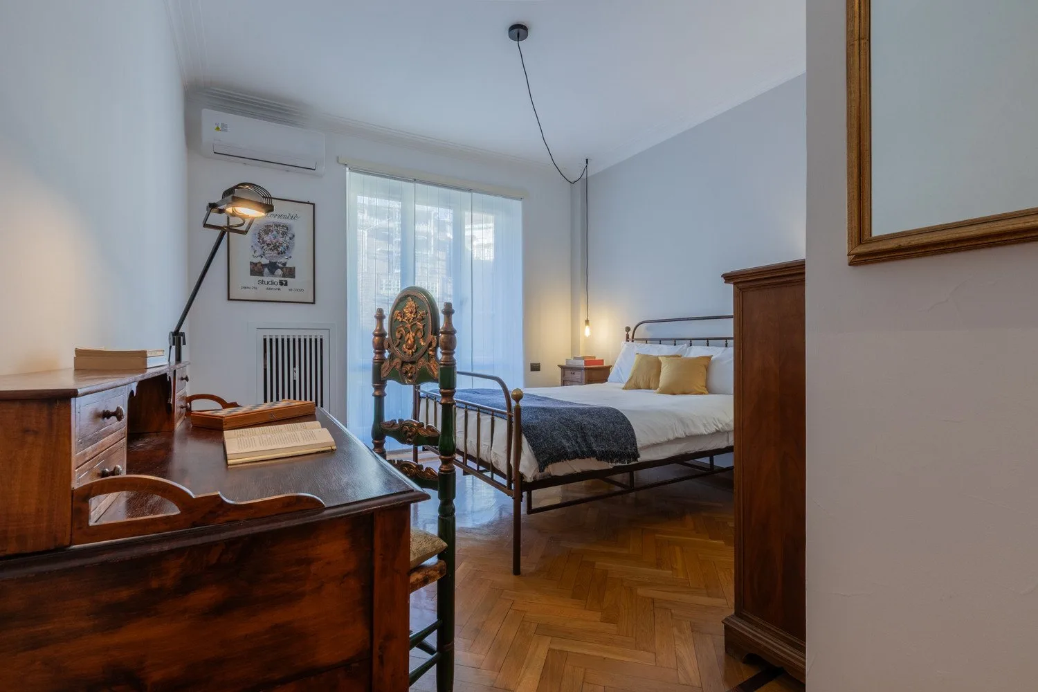 A bedroom with a bed, wooden desk, and tall windows.