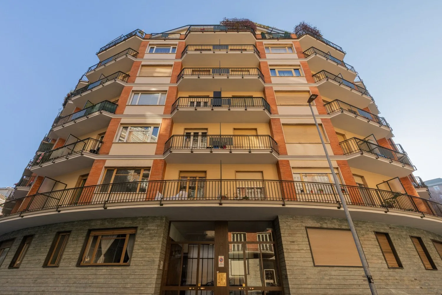 A multi-story apartment building with rows of balconies rises against a clear sky.