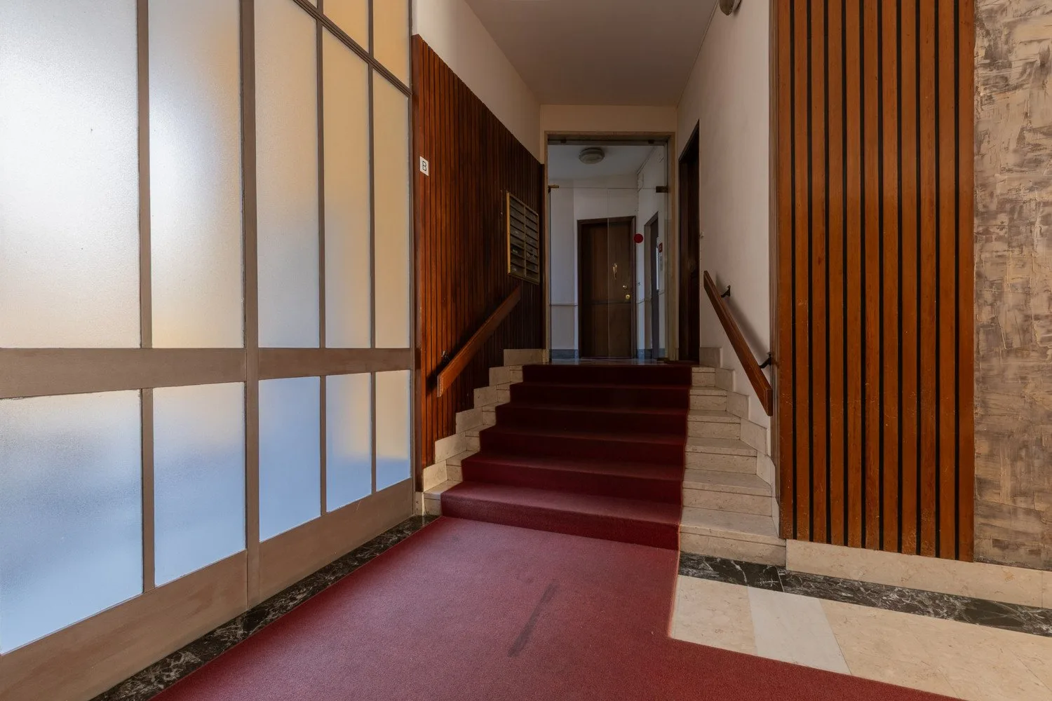 An interior hallway leads to a staircase with red carpeting and wood paneling.