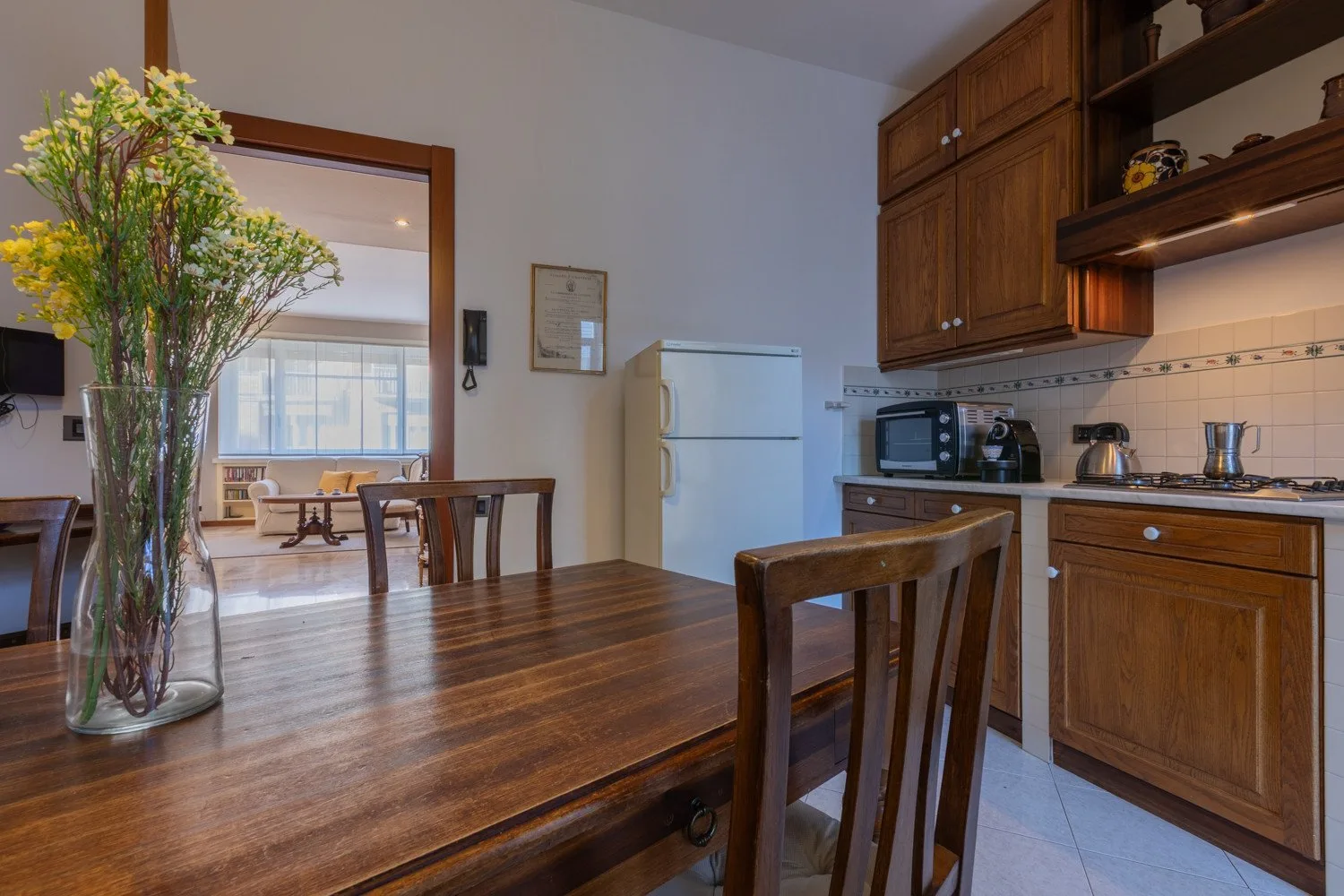 A dining area with a wooden table beside a kitchen with wooden cabinets.