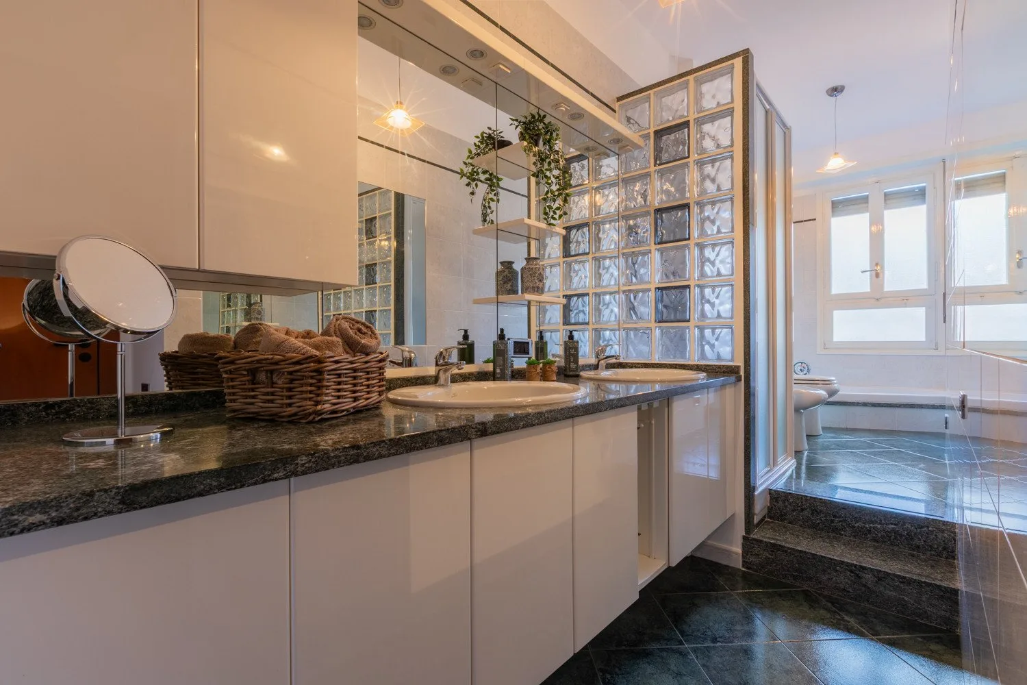 A bathroom vanity with a sink opens onto a bathtub beneath bright windows.