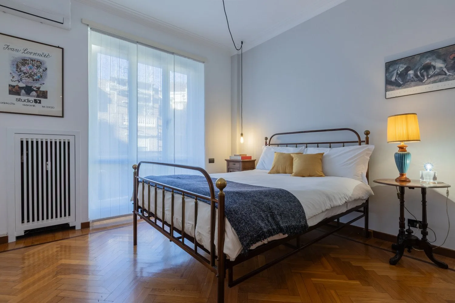 A bedroom with a metal bed, white bedding, and a bedside lamp.