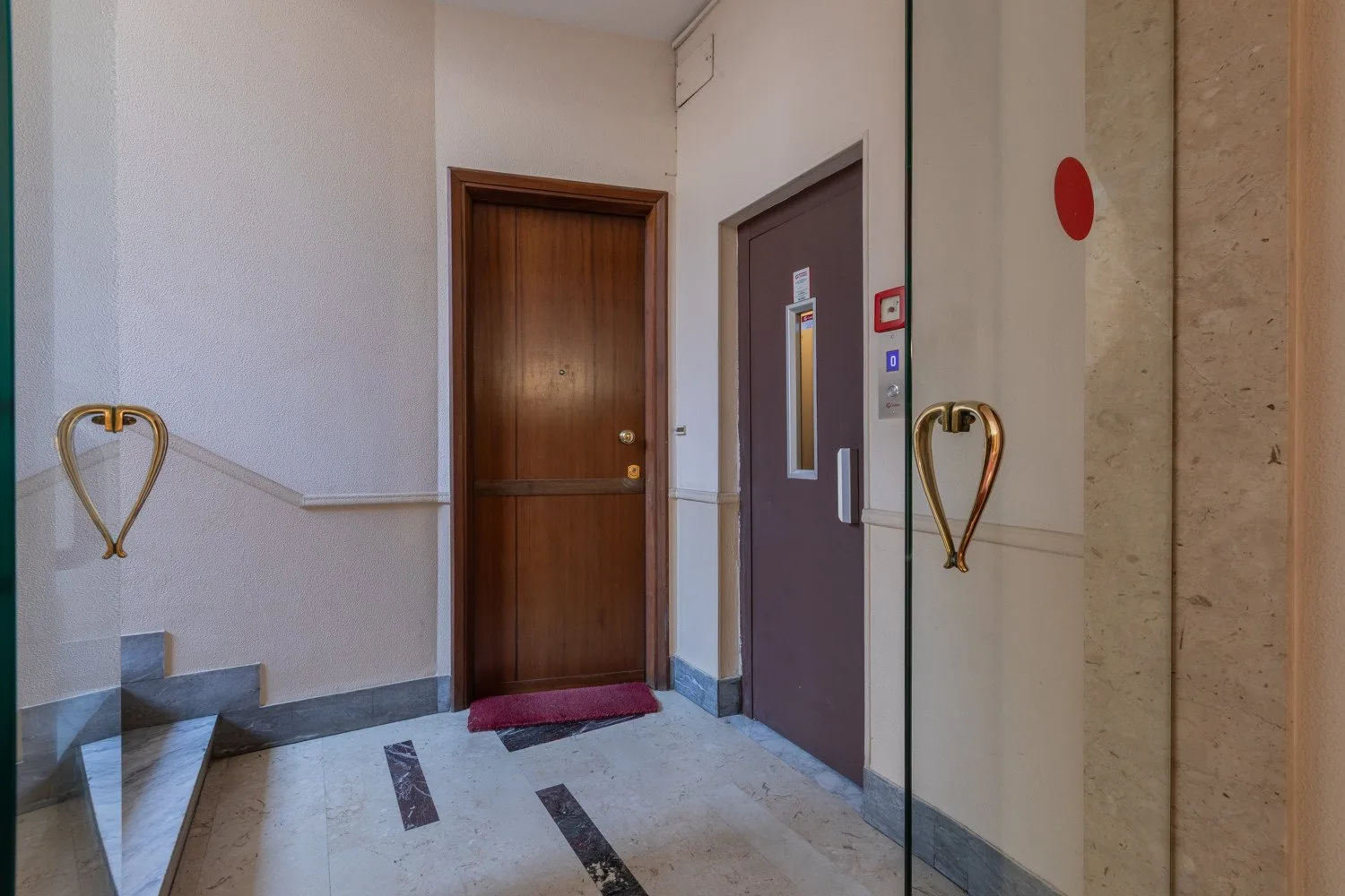An interior hallway with a wooden door, an elevator, and tiled flooring.