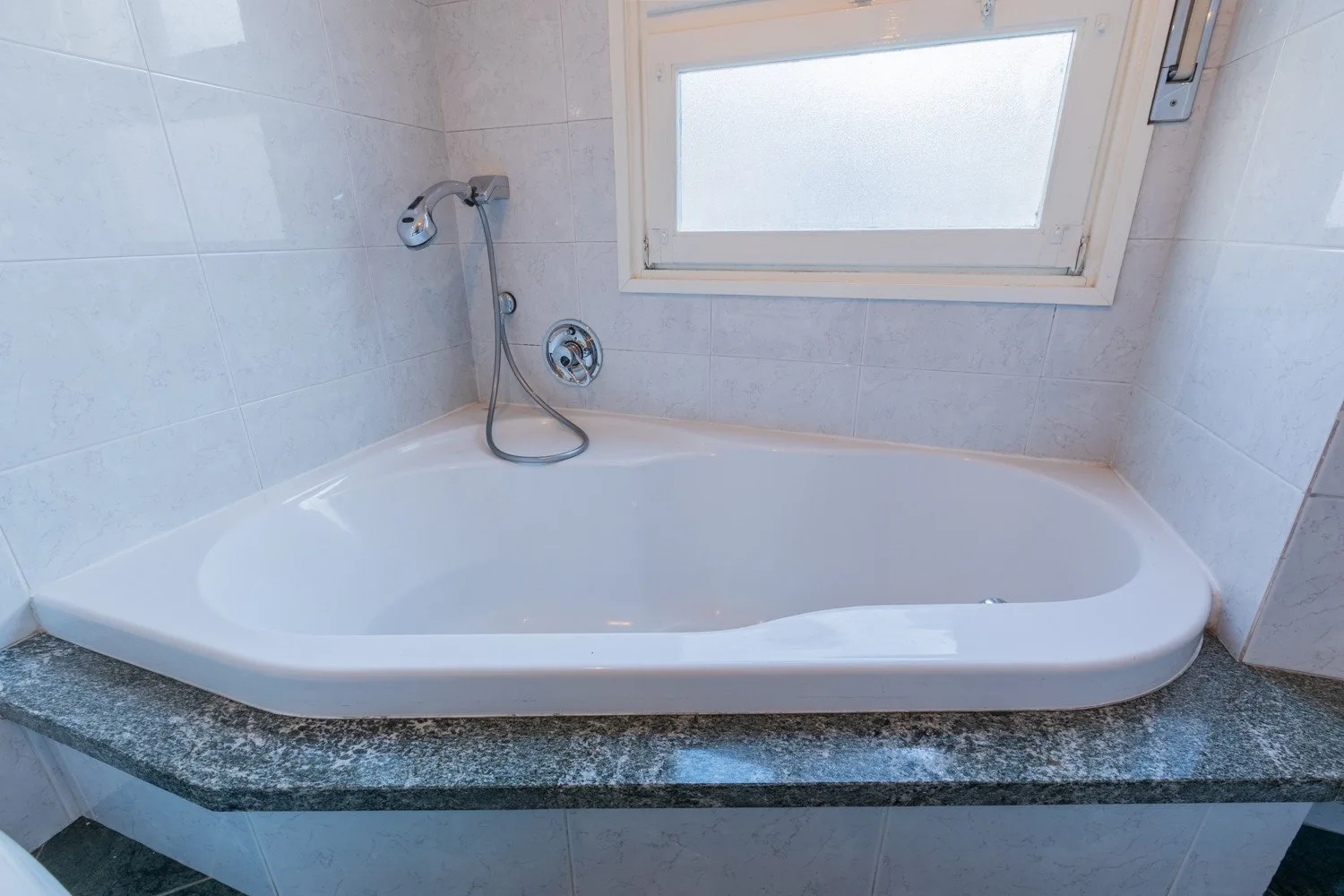 A bathroom with a bathtub beneath a frosted window.