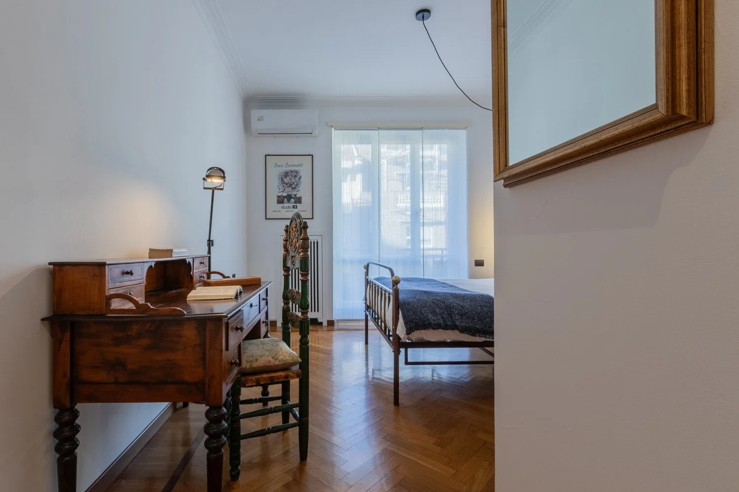 A bedroom with a wooden desk and a bed beside the window.