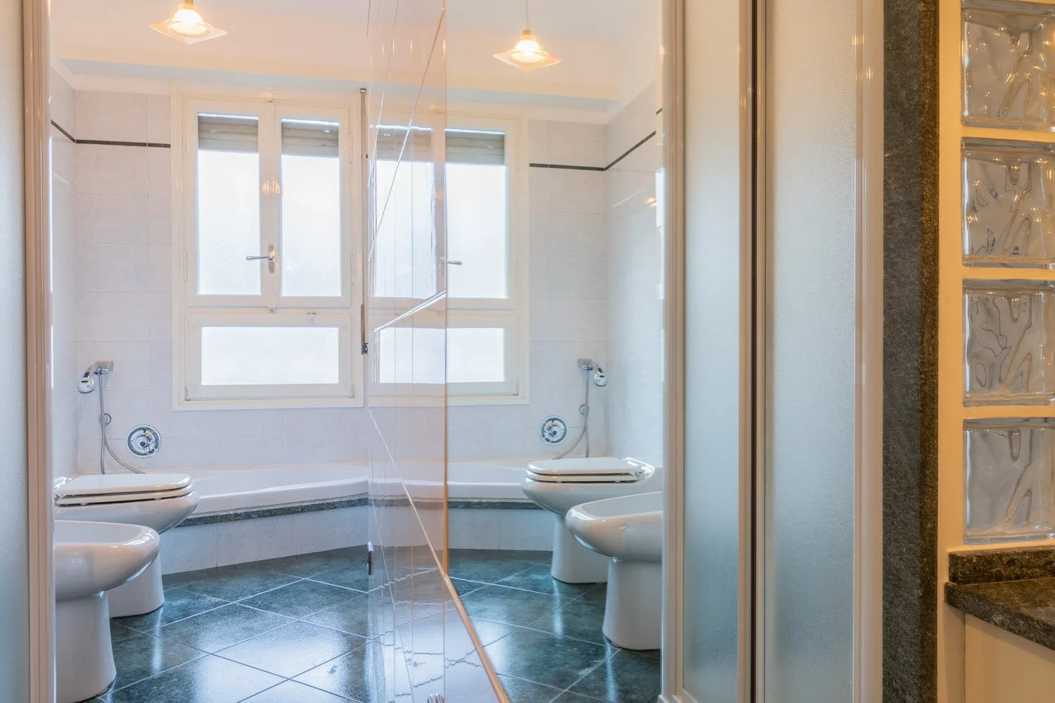 A tiled bathroom with a bathtub, toilet, and bright windows.