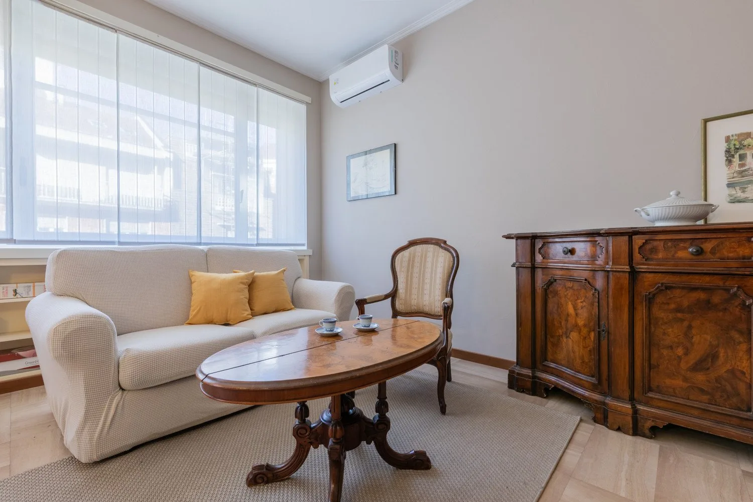 A sitting room has a sofa, an oval coffee table, and a wooden cabinet.