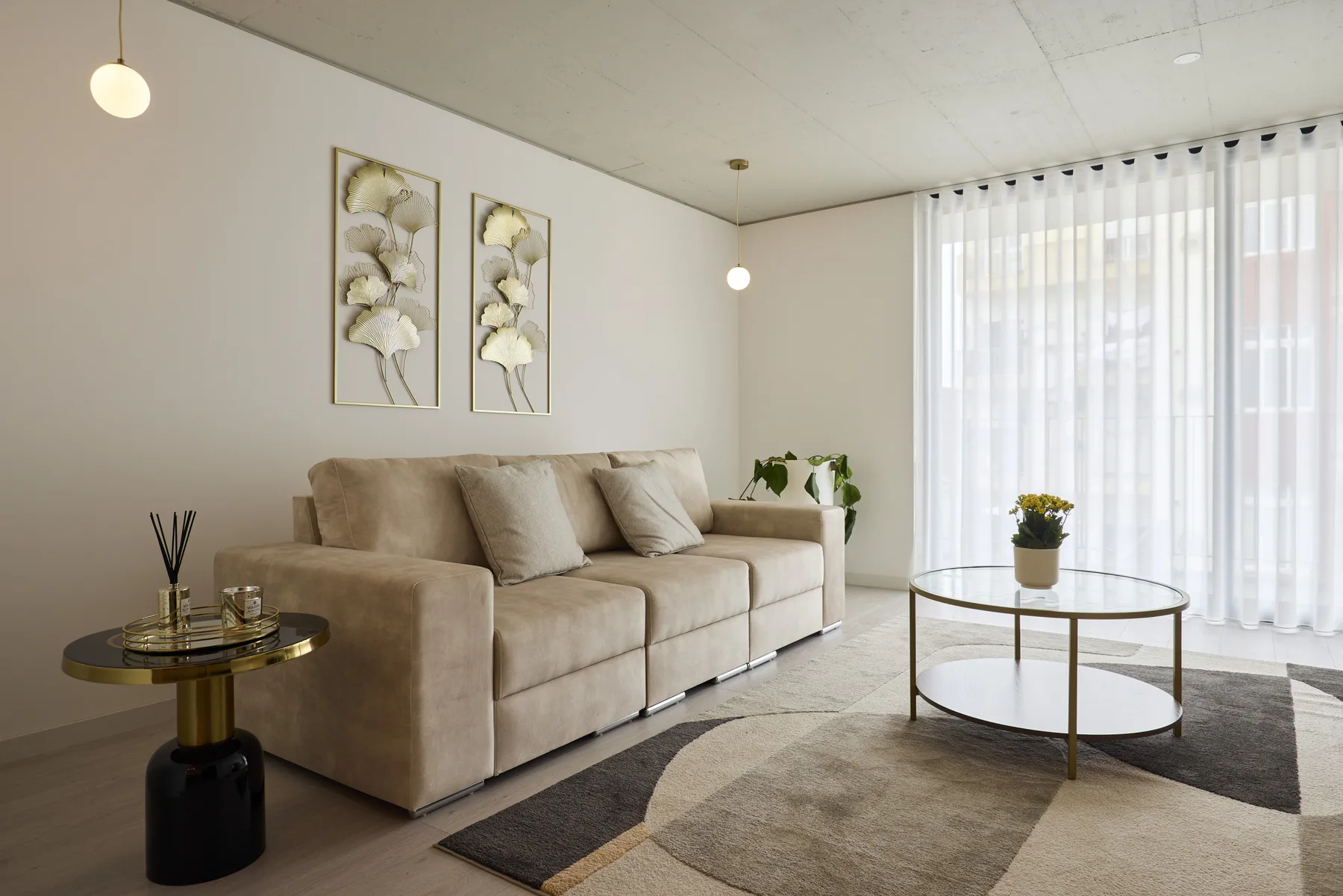 A bright living room with beige seating, framed artwork, and sheer curtains.