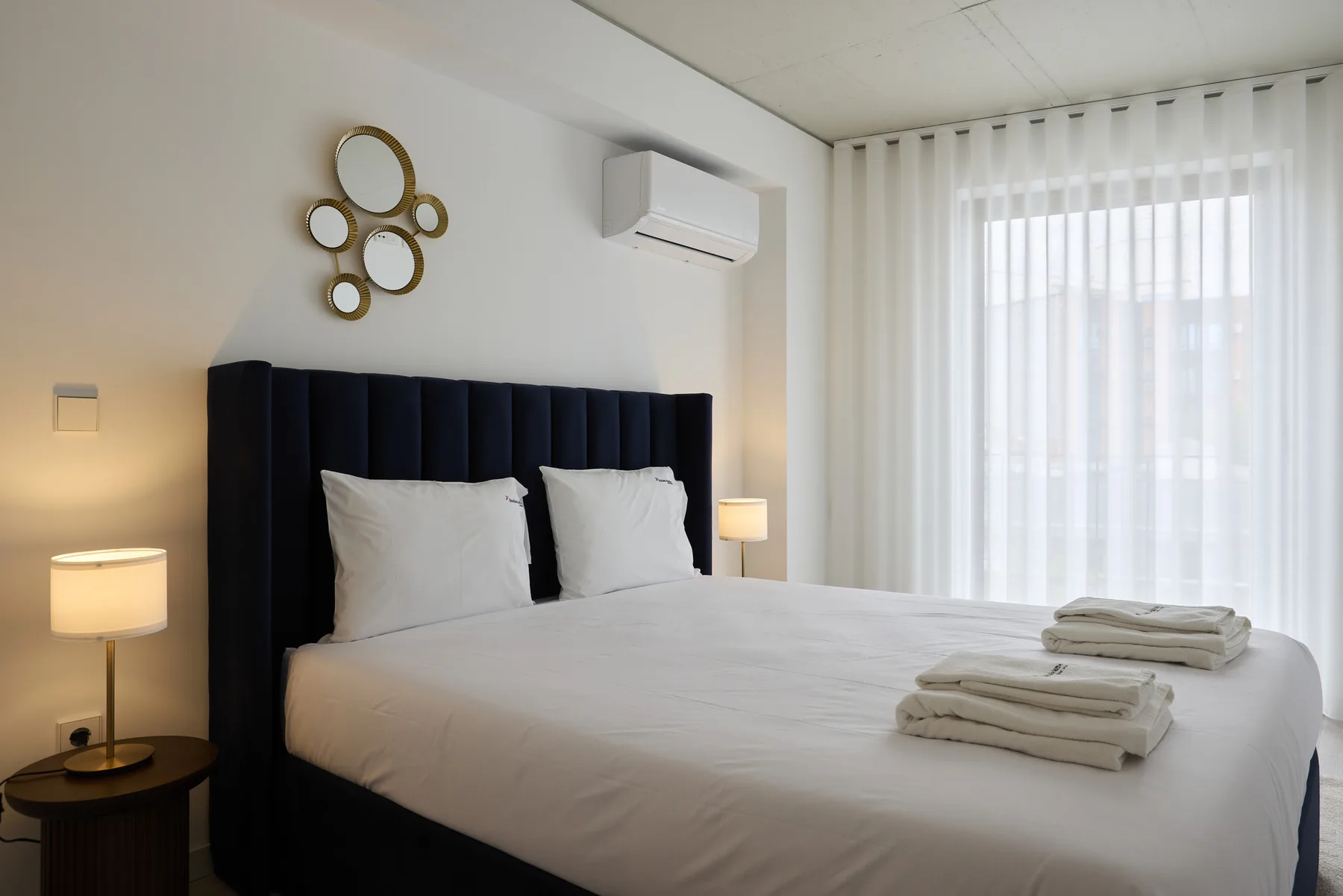 A bedroom with a neatly made bed and sheer curtains.