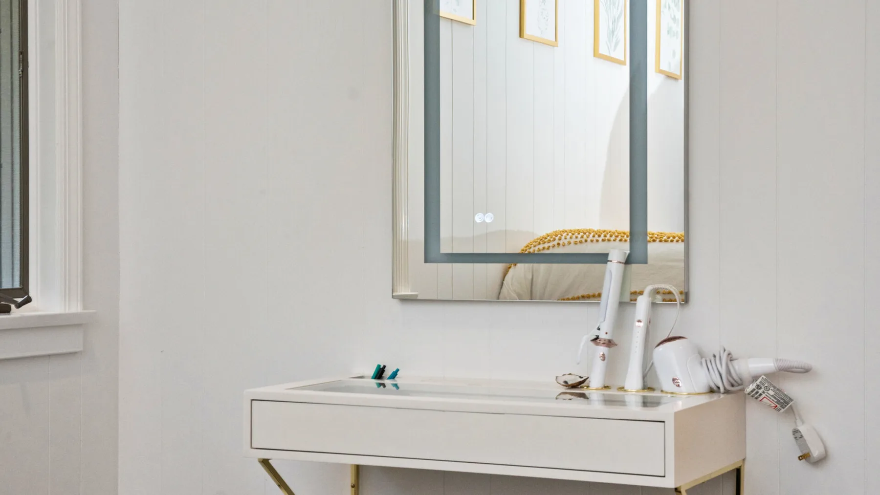 Un lavabo de baño luminoso con espejo y algunos artículos de aseo sobre la encimera.